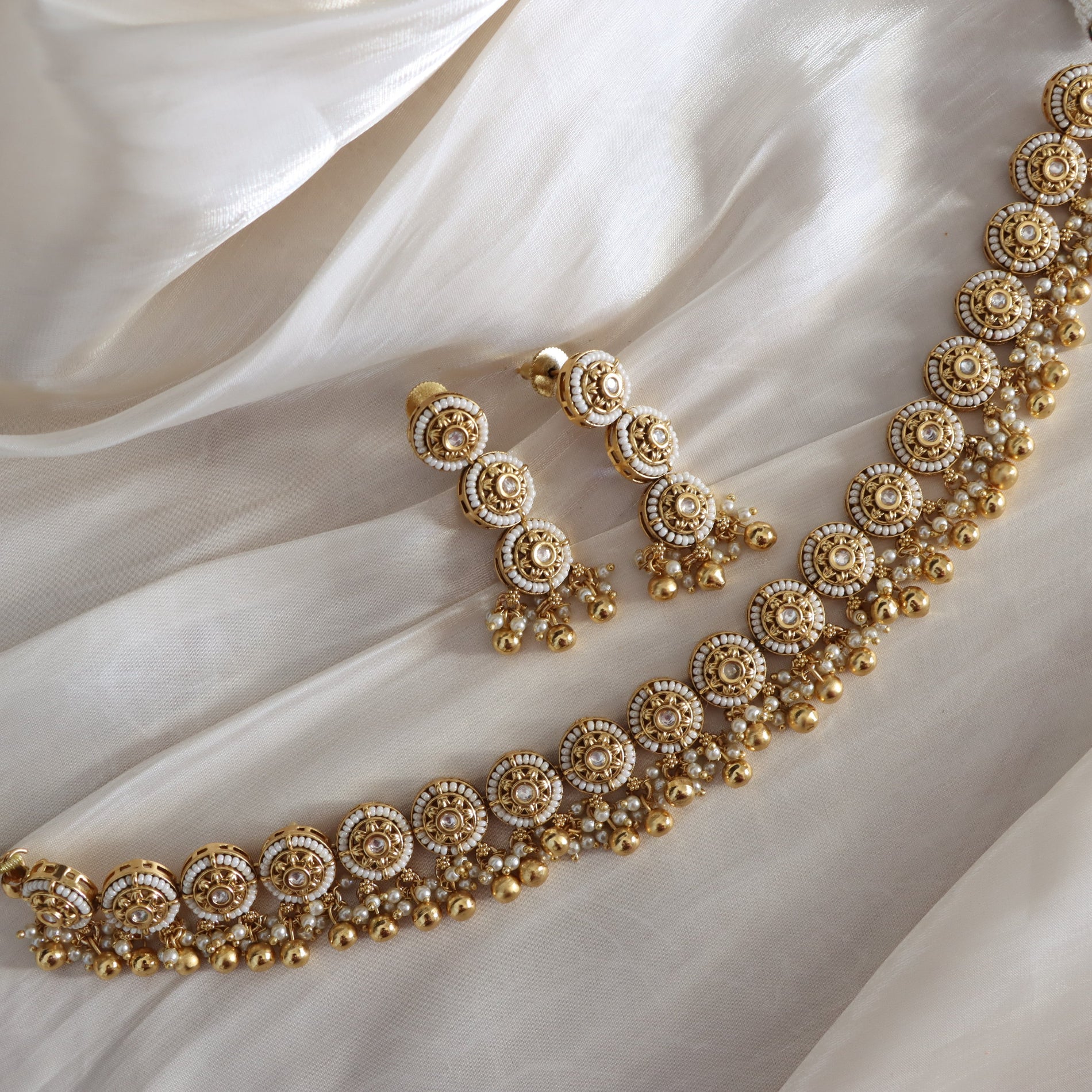 Gold jewelry set with necklace and earrings on a white fabric background