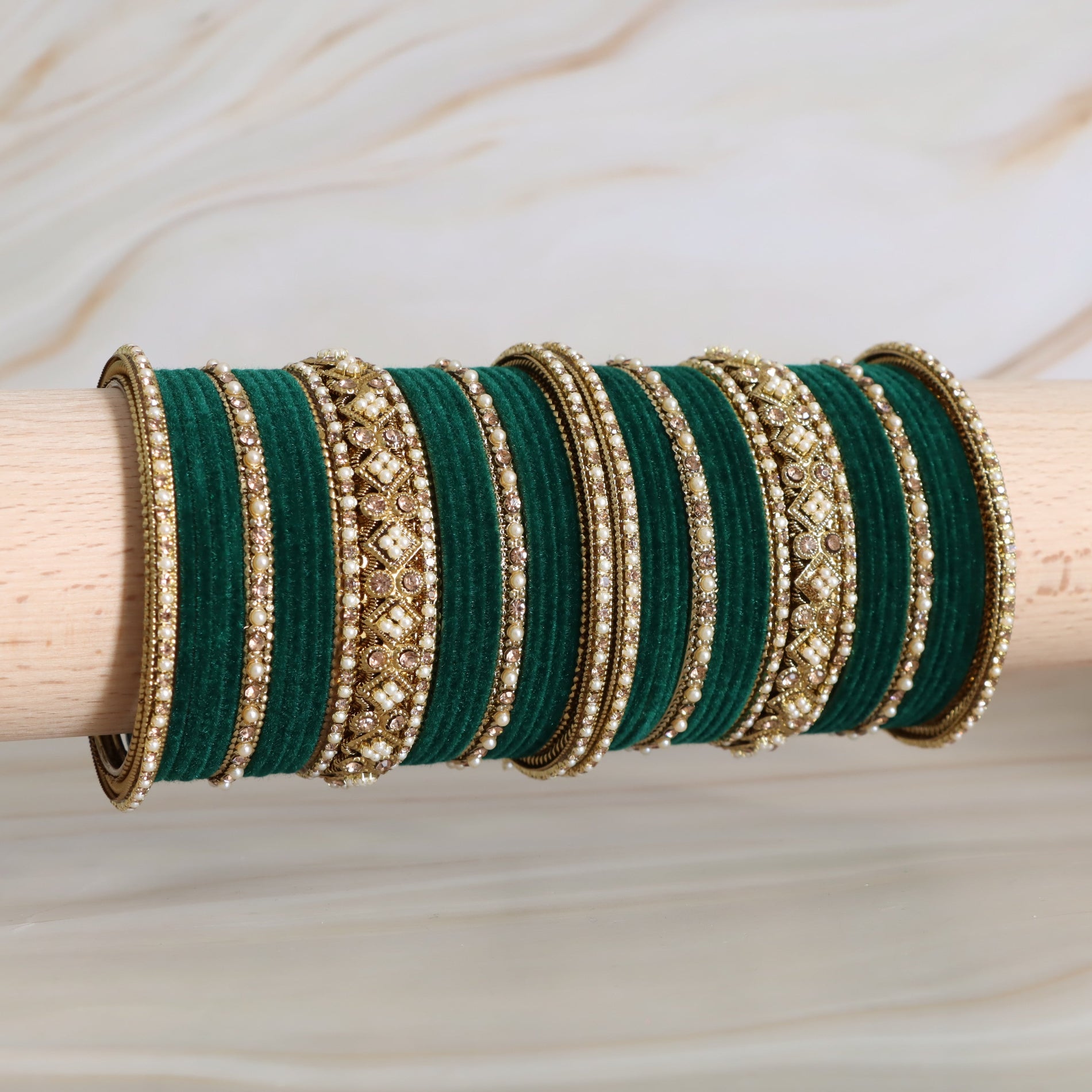 Set of green and gold bangles on a wooden stick with a neutral background
