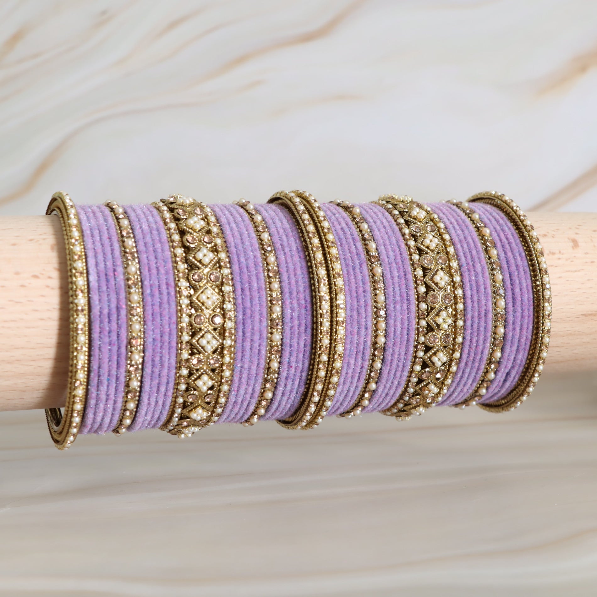 Purple and gold bangles on a wooden stick with a neutral background