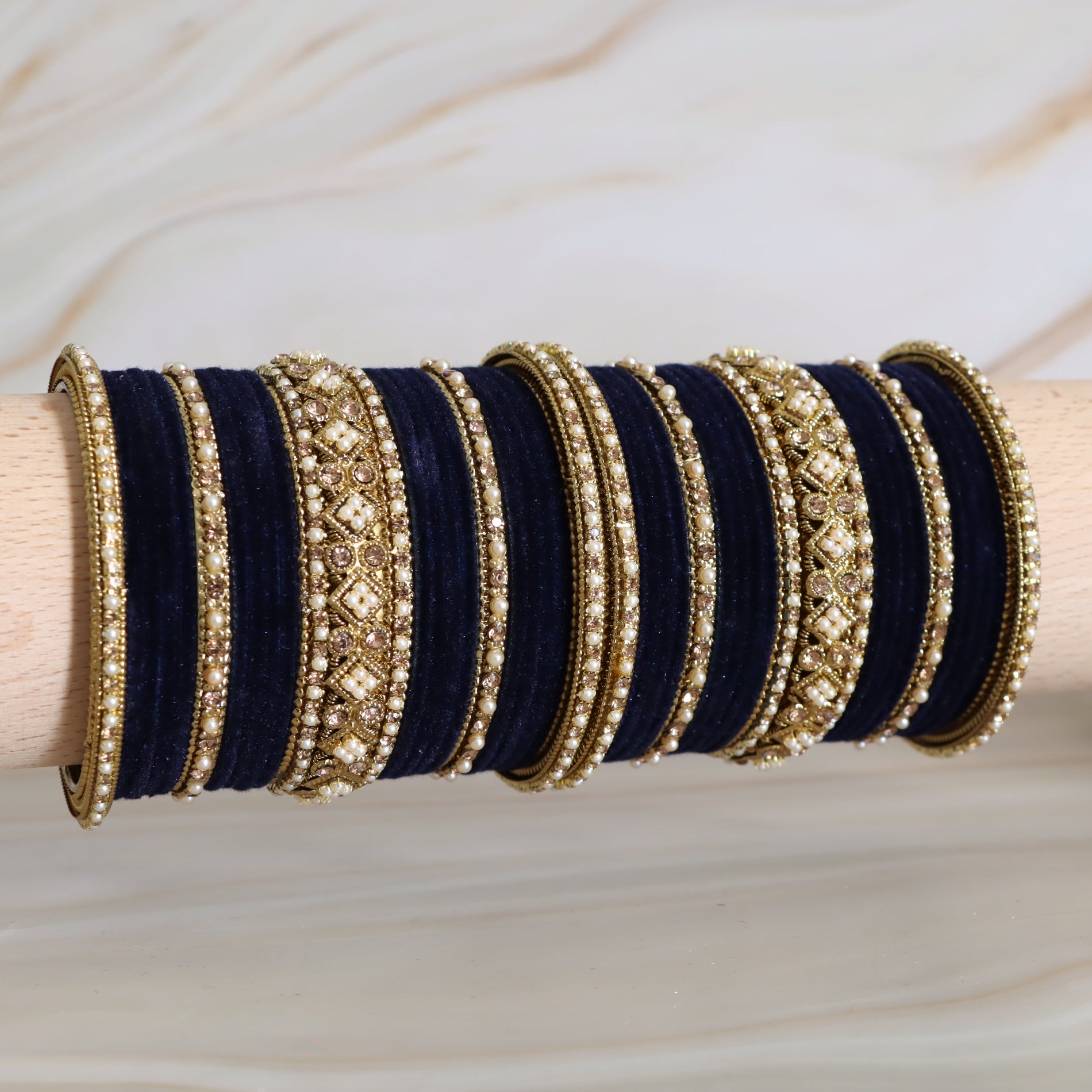 Set of navy blue and gold bangles on a wooden stick against a neutral background