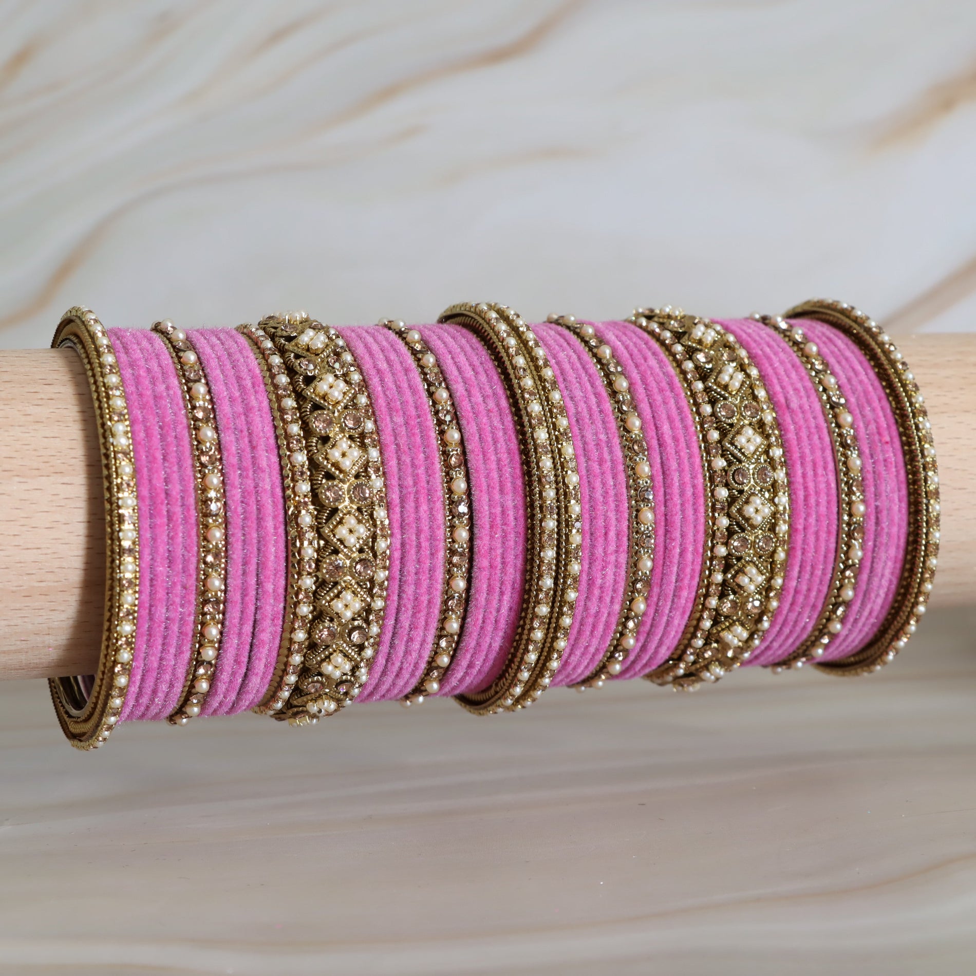 Pink bangles with gold detailing on a wooden stick against a neutral background
