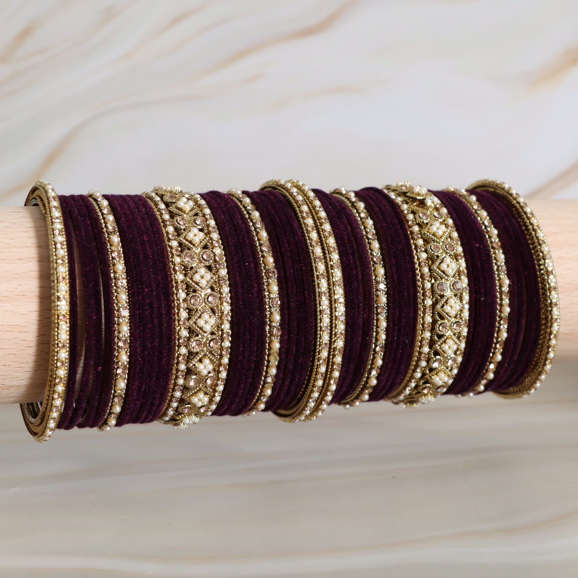 Set of purple and gold bangles on a wooden stick against a neutral background