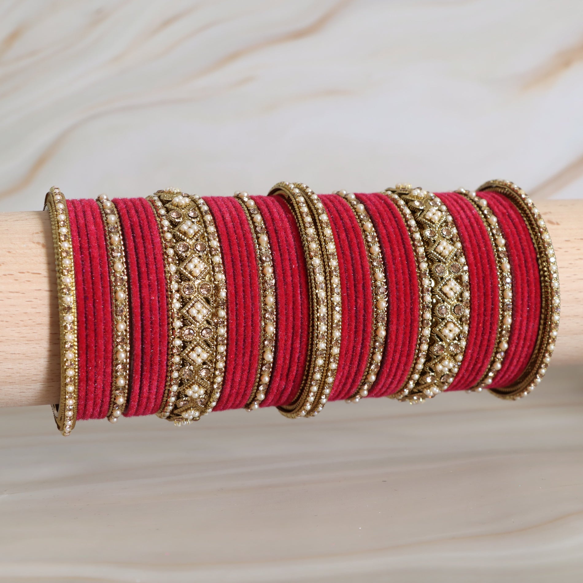 Red and gold bangles on a wooden stick against a neutral background