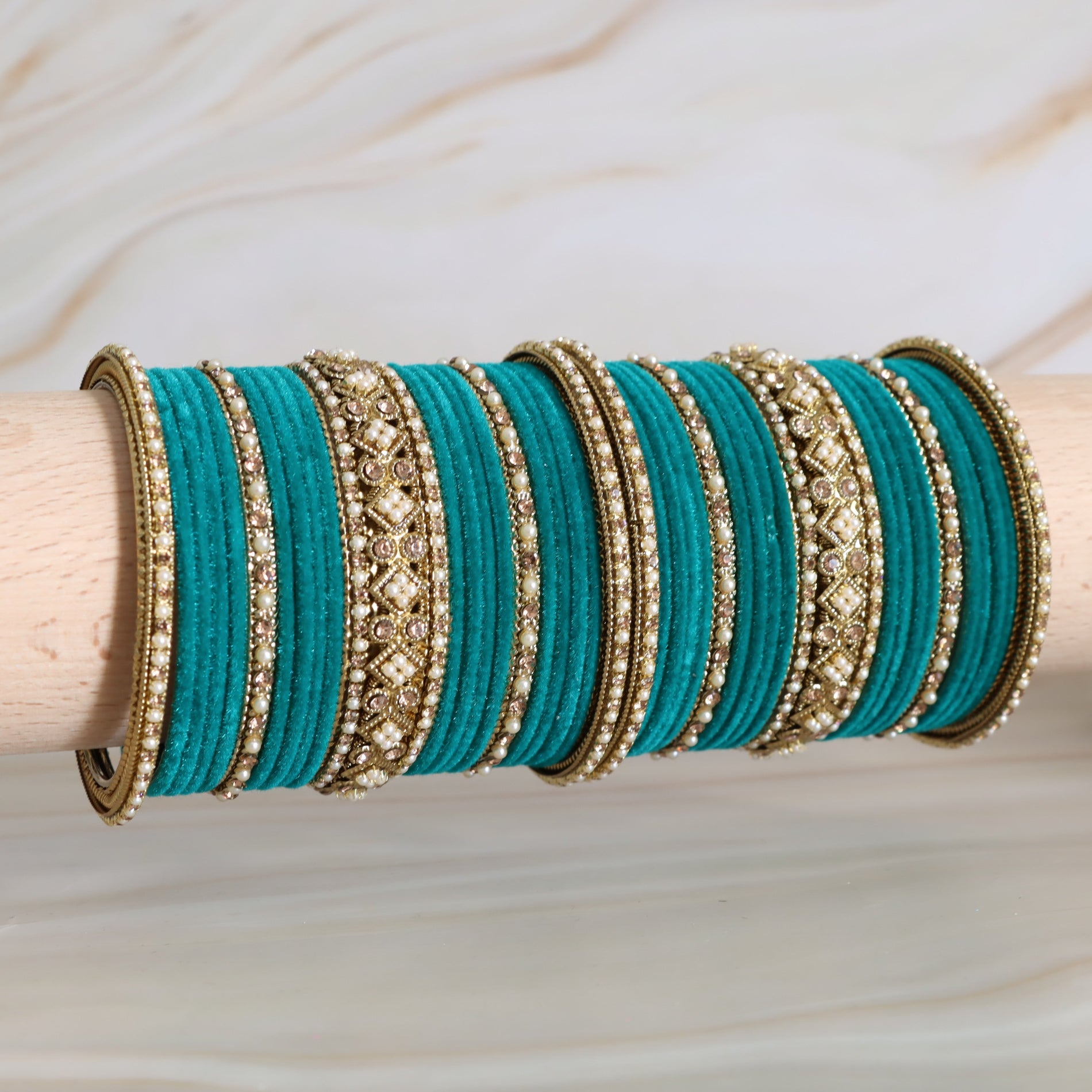 Turquoise bangles with gold detailing on a wooden stick against a neutral background