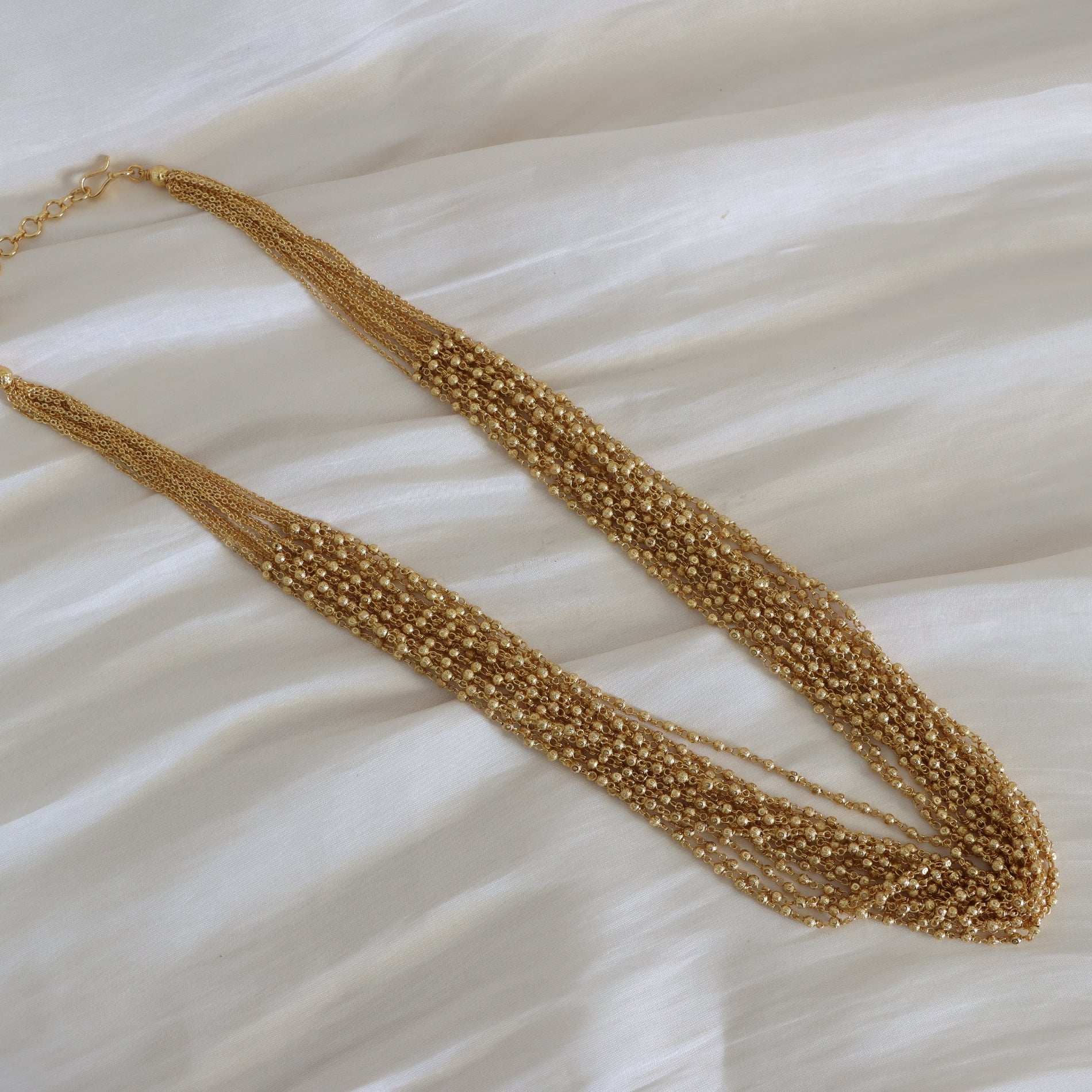 Gold beaded necklace on a textured white surface