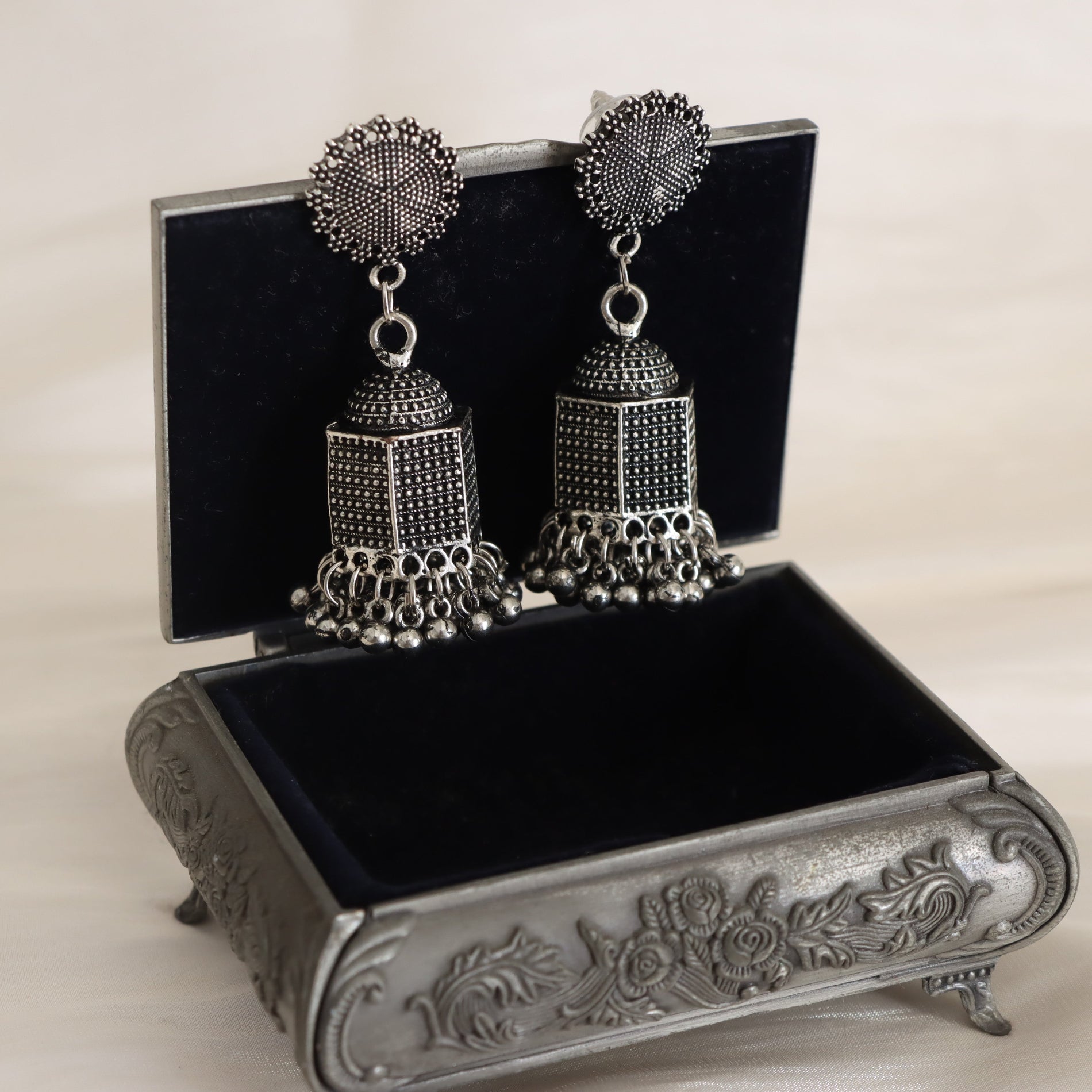 Silver earrings on a decorative black jewelry box with floral designs.