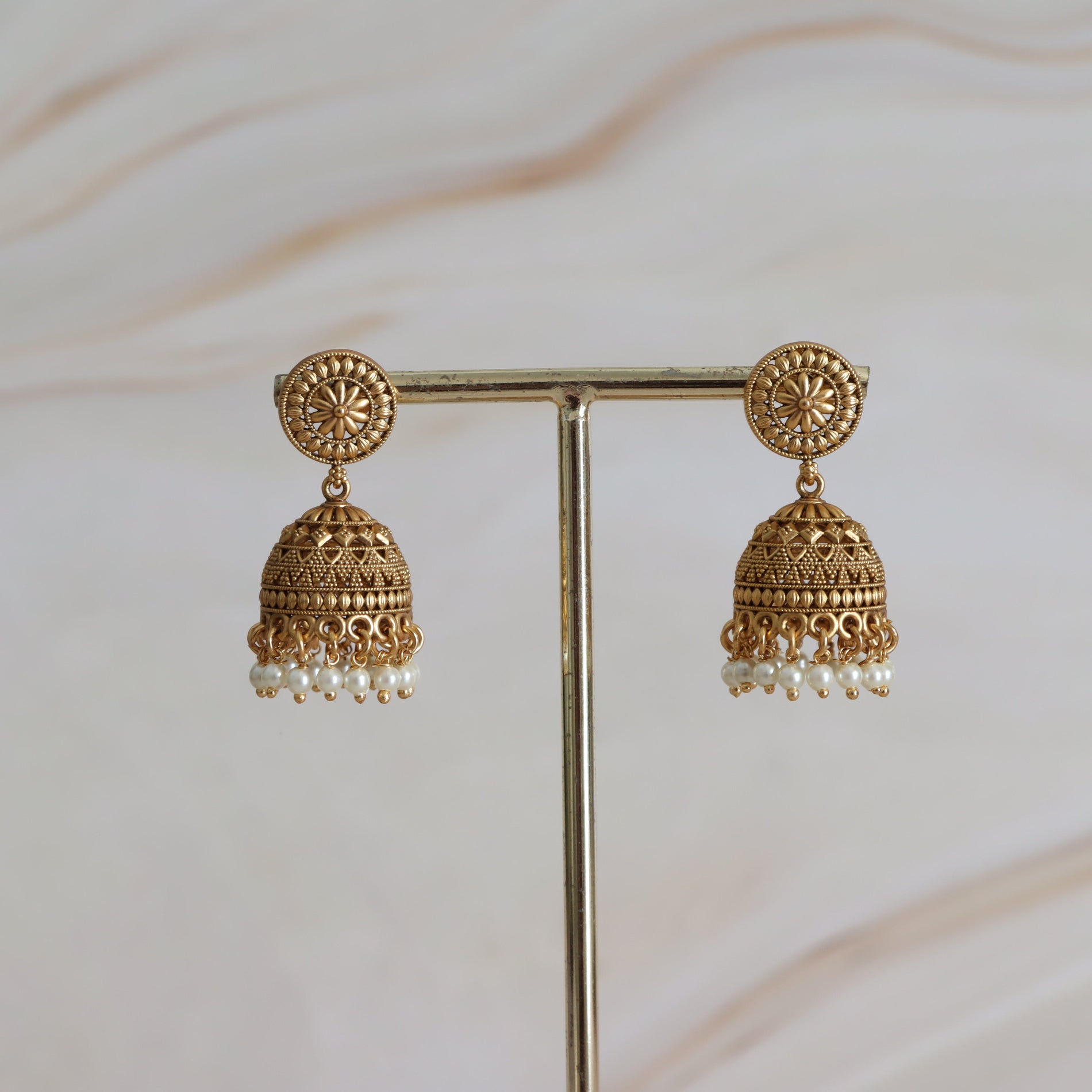 Pair of gold earrings with pearl drops on a stand against a neutral background