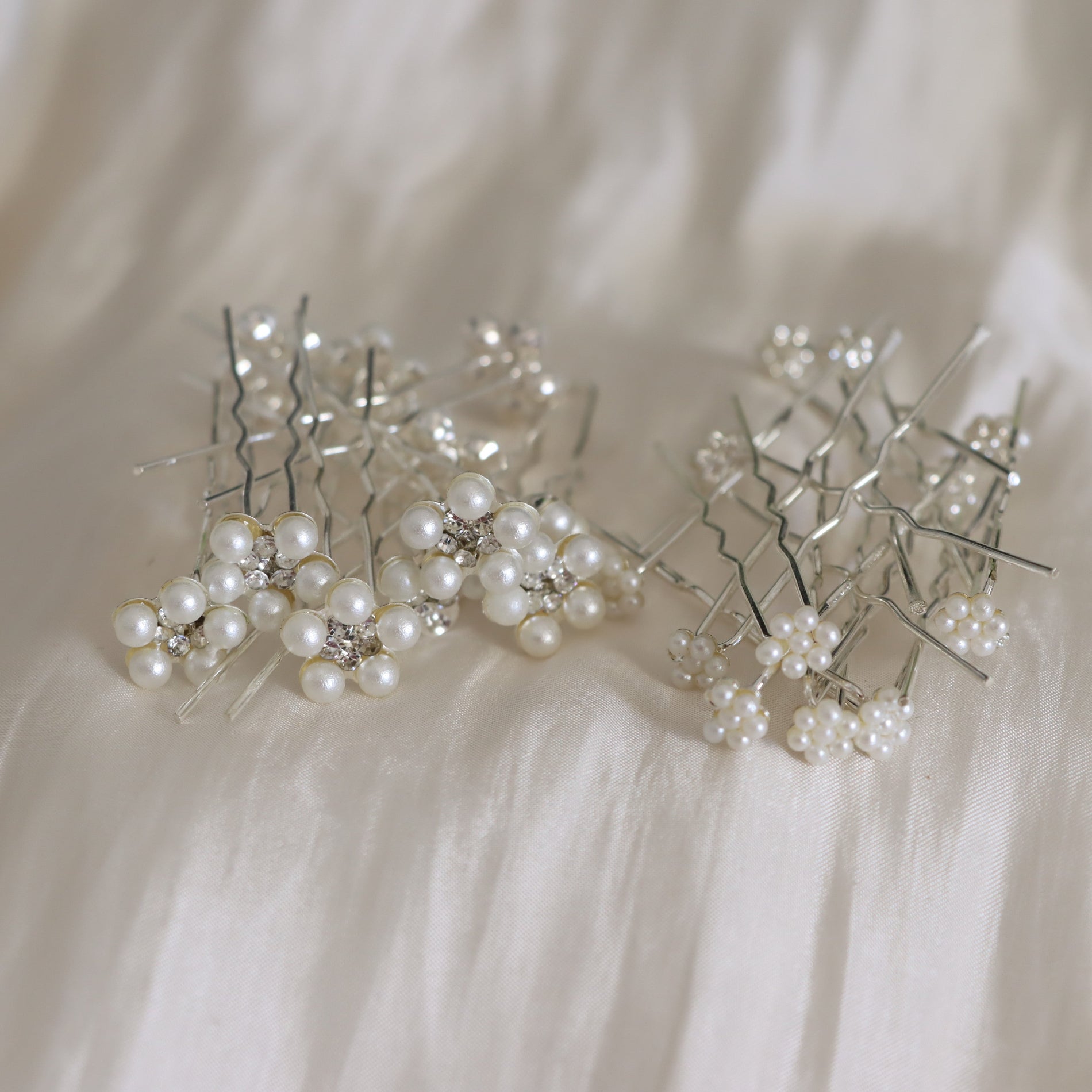 Two clusters of silver hair pins adorned with small white pearls and clear rhinestone accents, arranged on a soft white fabric background.