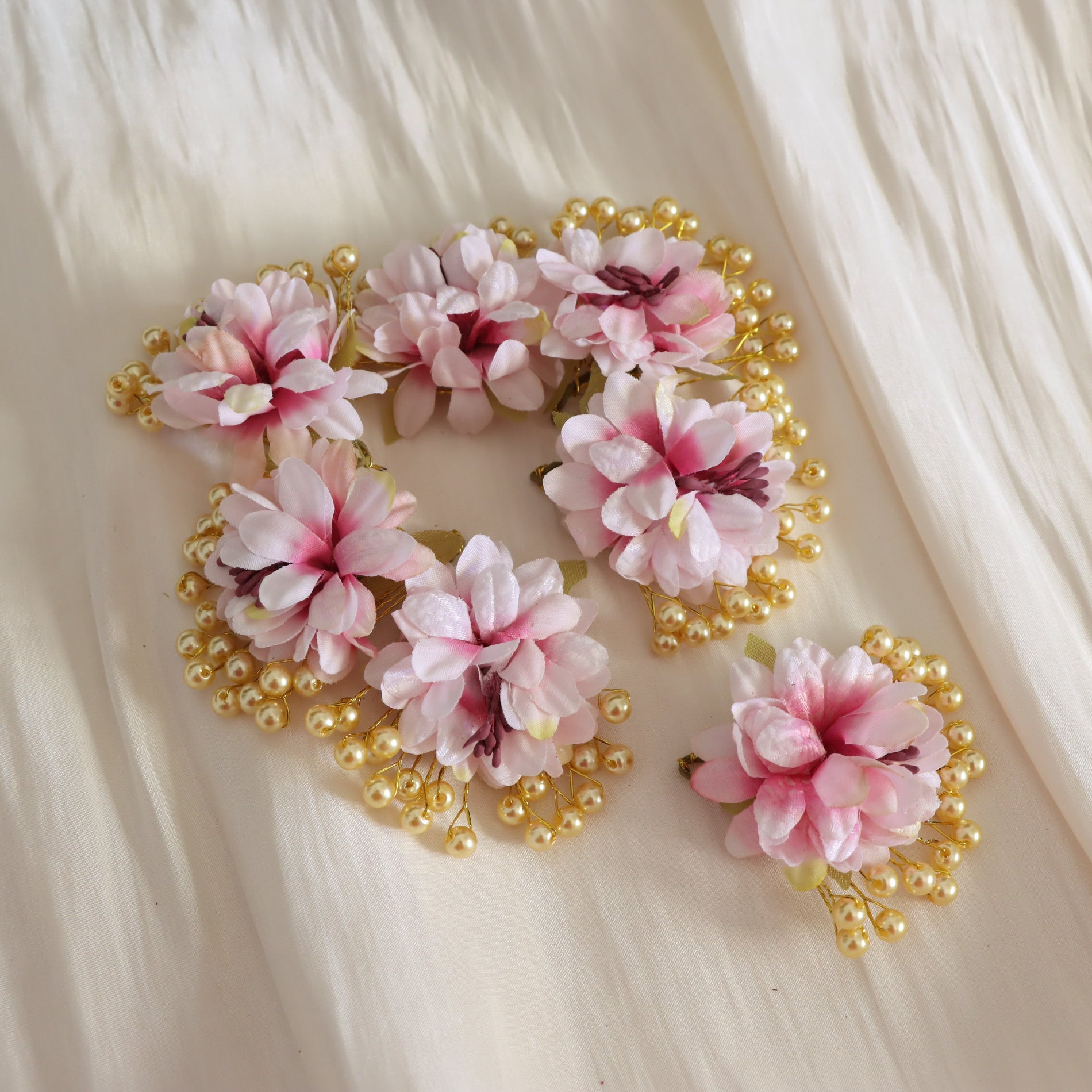 seven-piece pink artificial flower hair accessory set with gold pearl beads, displayed on a cream-colored textured fabric background.
