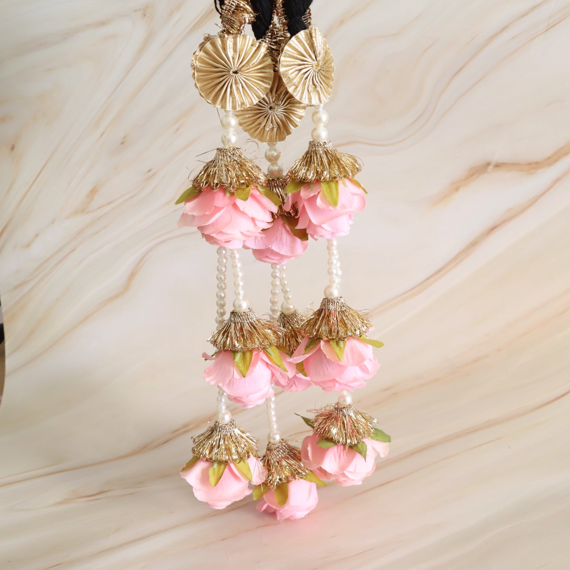 Decorative hanging with pink flowers and gold accents on a marble background