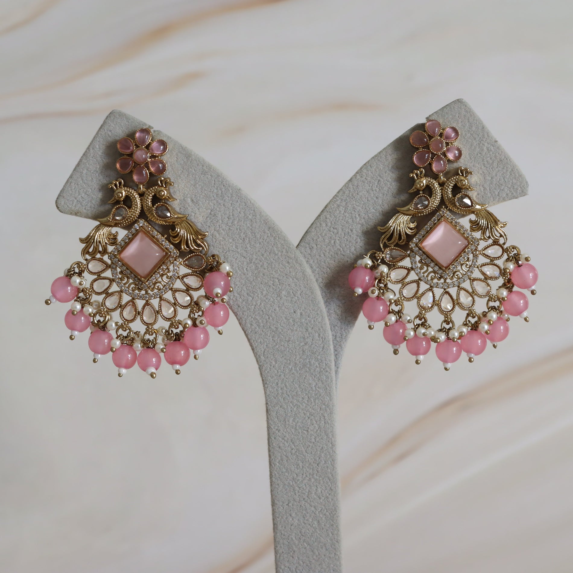 Ornate earrings with pink beads on a neutral background