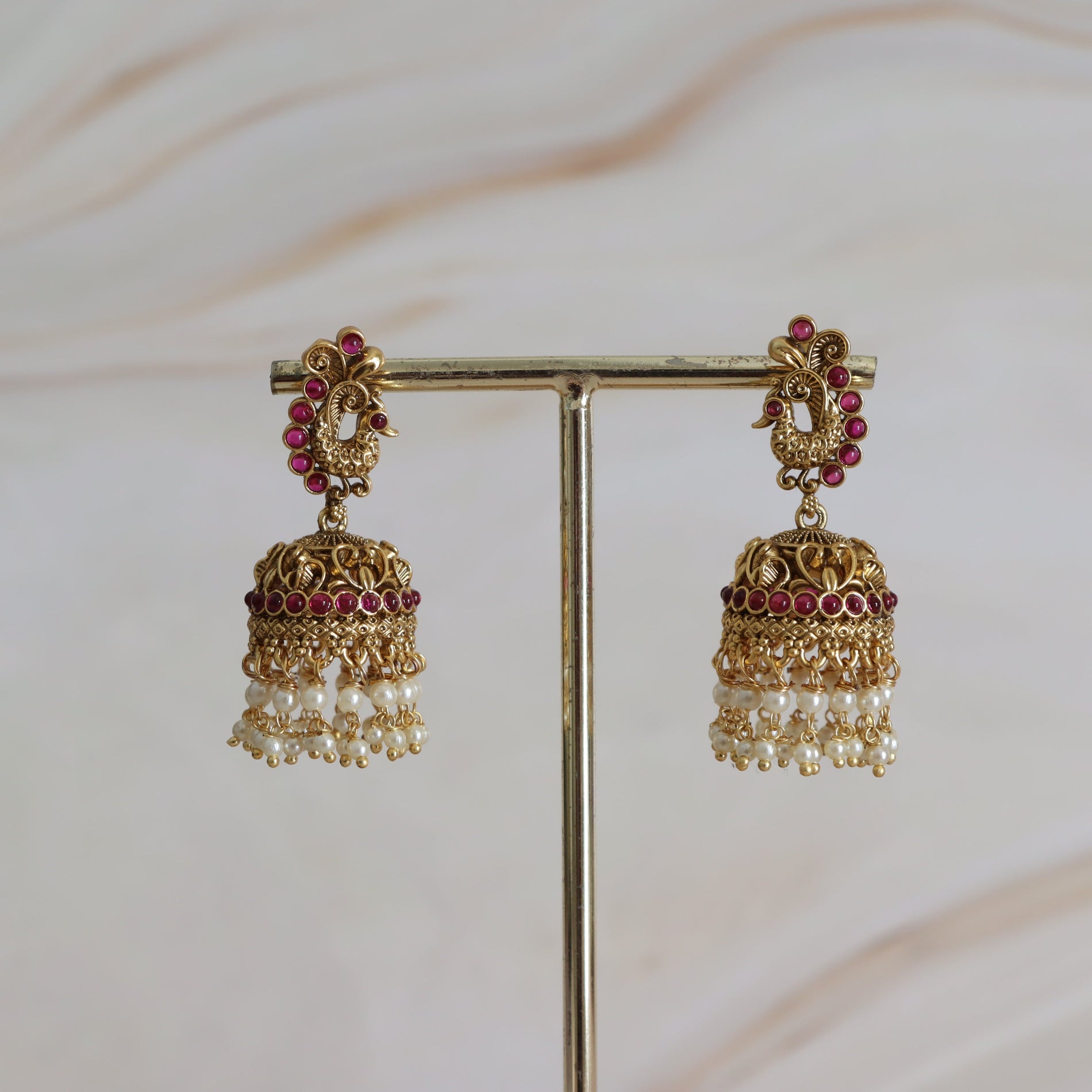 Pair of gold and red earrings on a stand with a soft background