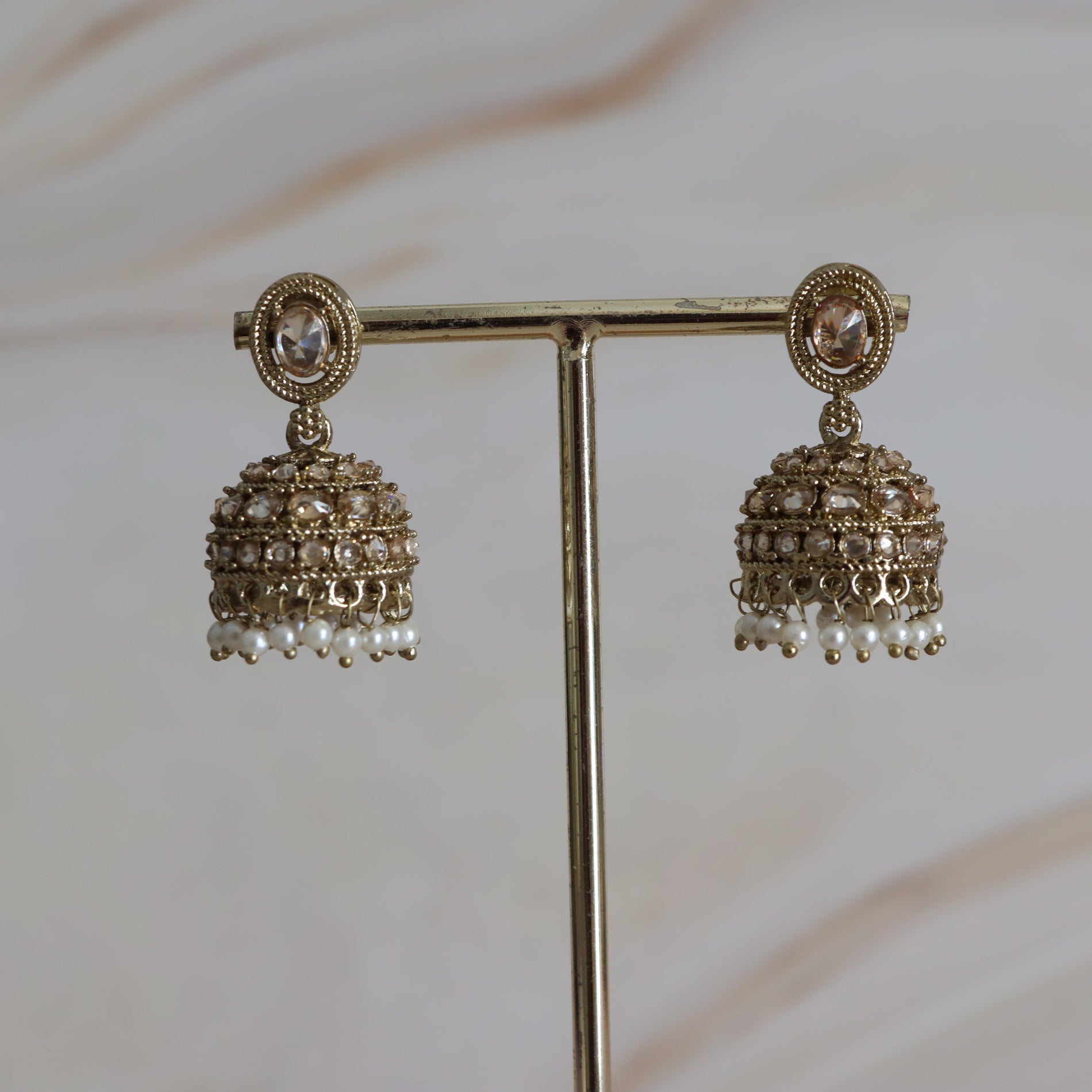 Pair of gold earrings with intricate designs on a stand against a neutral background