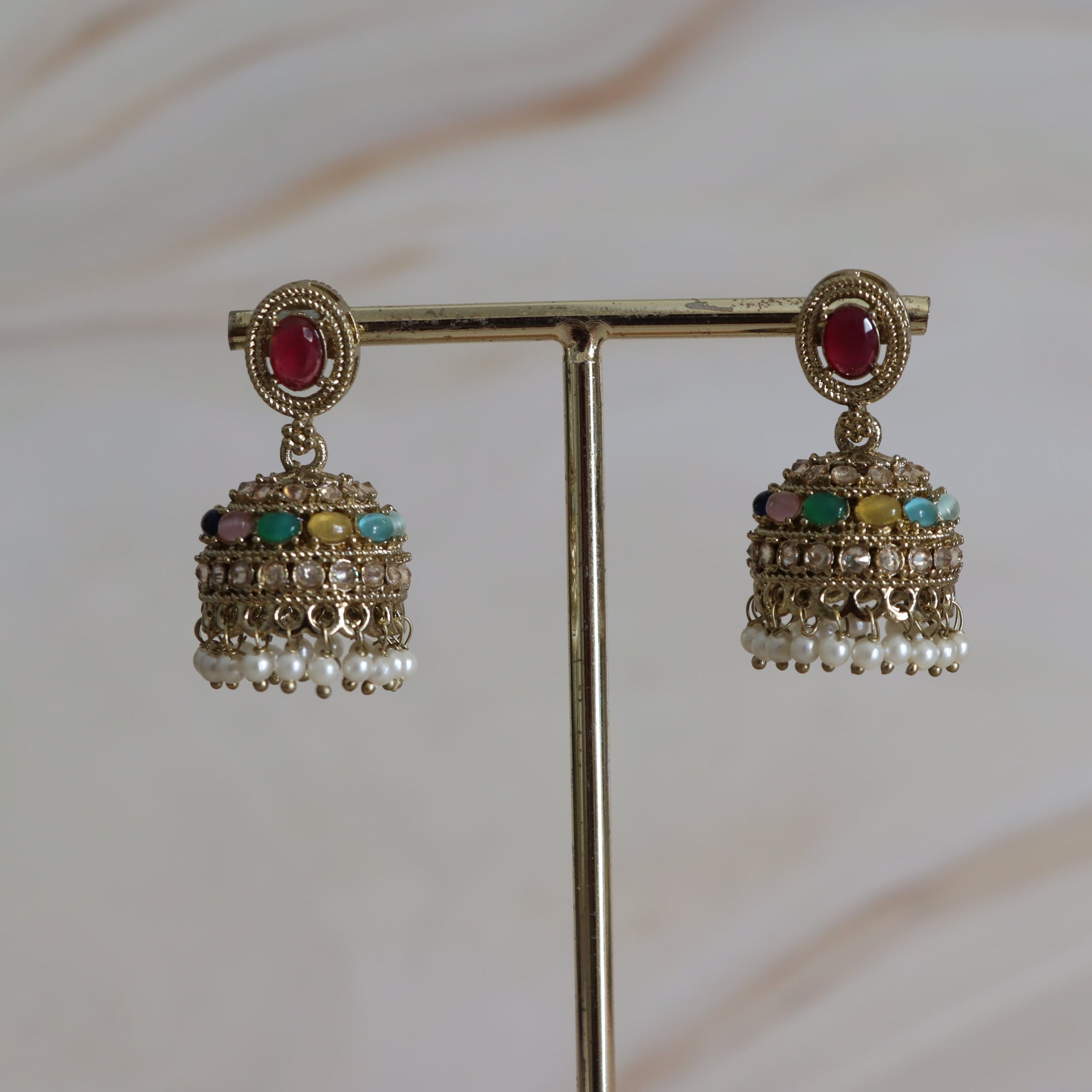 Pair of gold earrings with gemstones on a stand against a neutral background