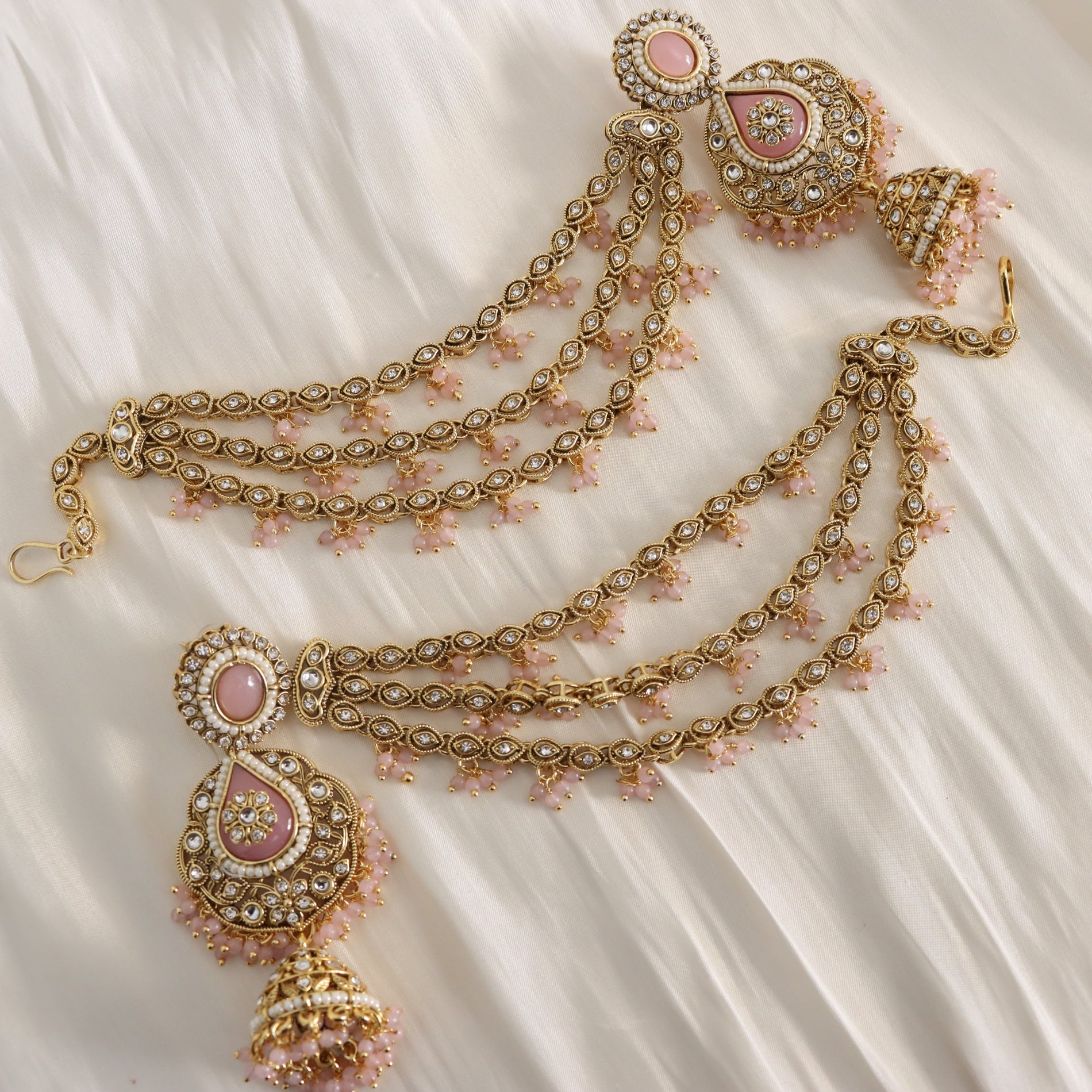 Ornate gold necklace with pink stones on a white fabric background