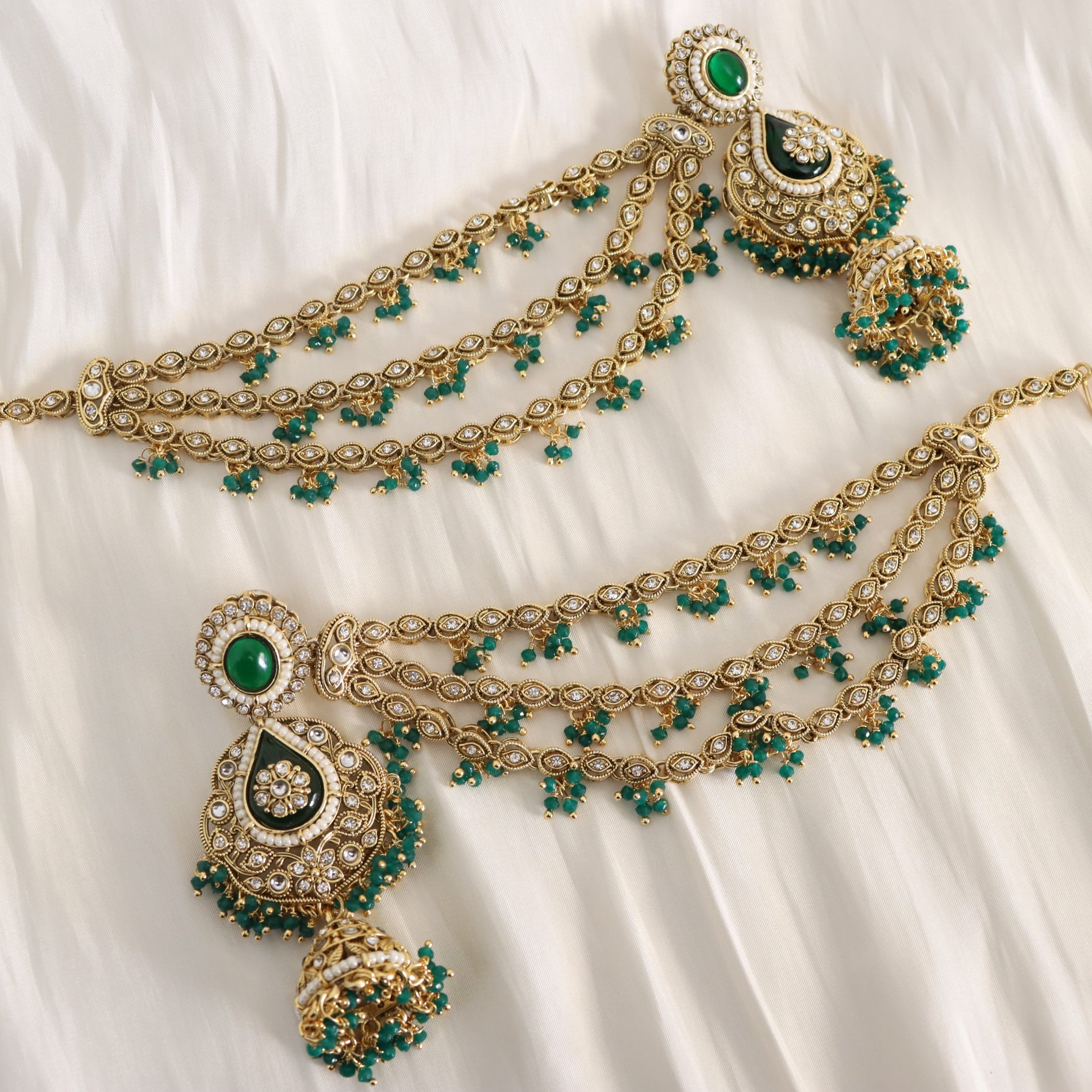 Ornate gold necklace with green gemstones on a white fabric background
