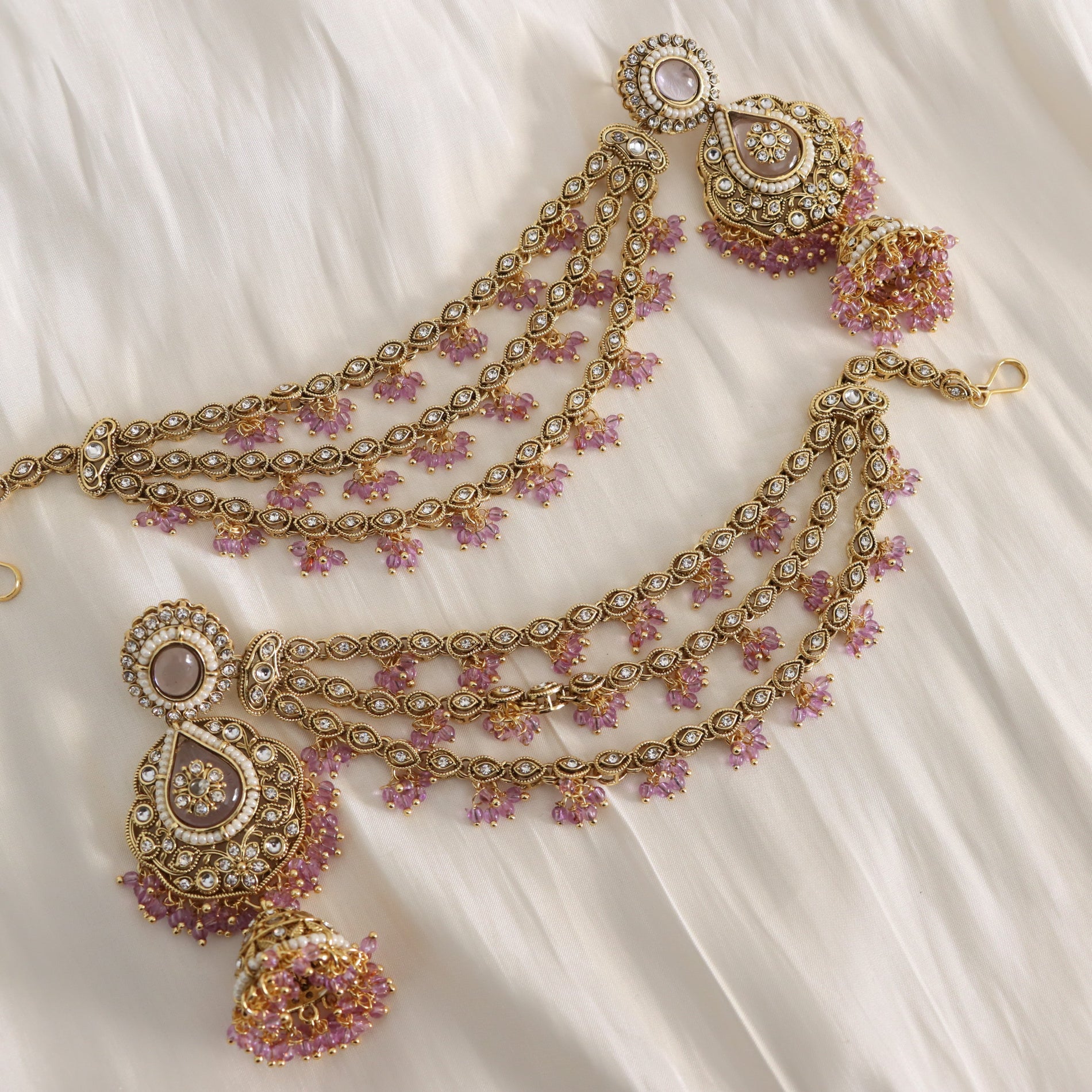 Ornate gold necklace with pink stones on a white fabric background
