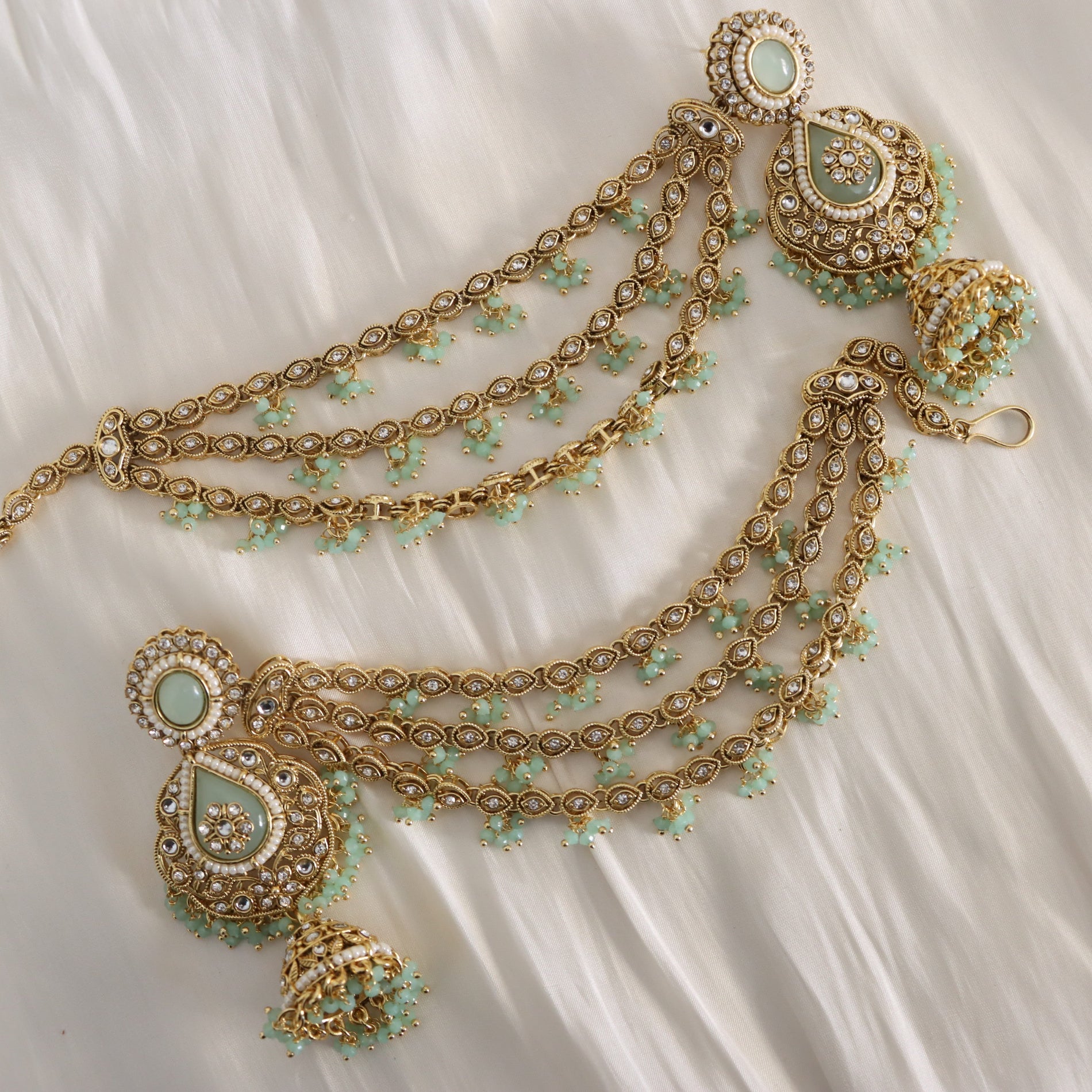 Gold and green jewelry set on a white fabric background