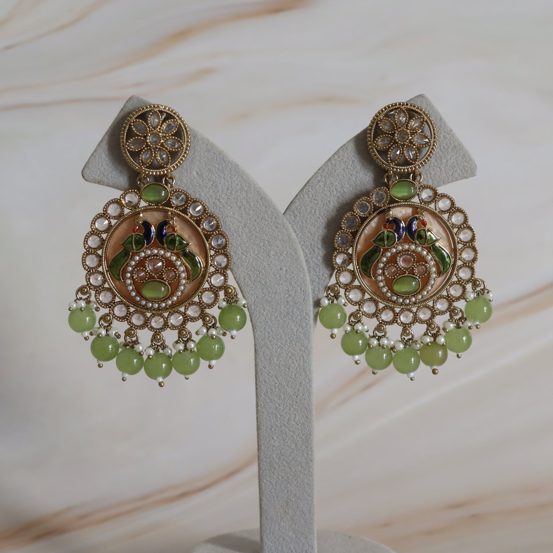 Pair of ornate earrings with green beads on a white stand.