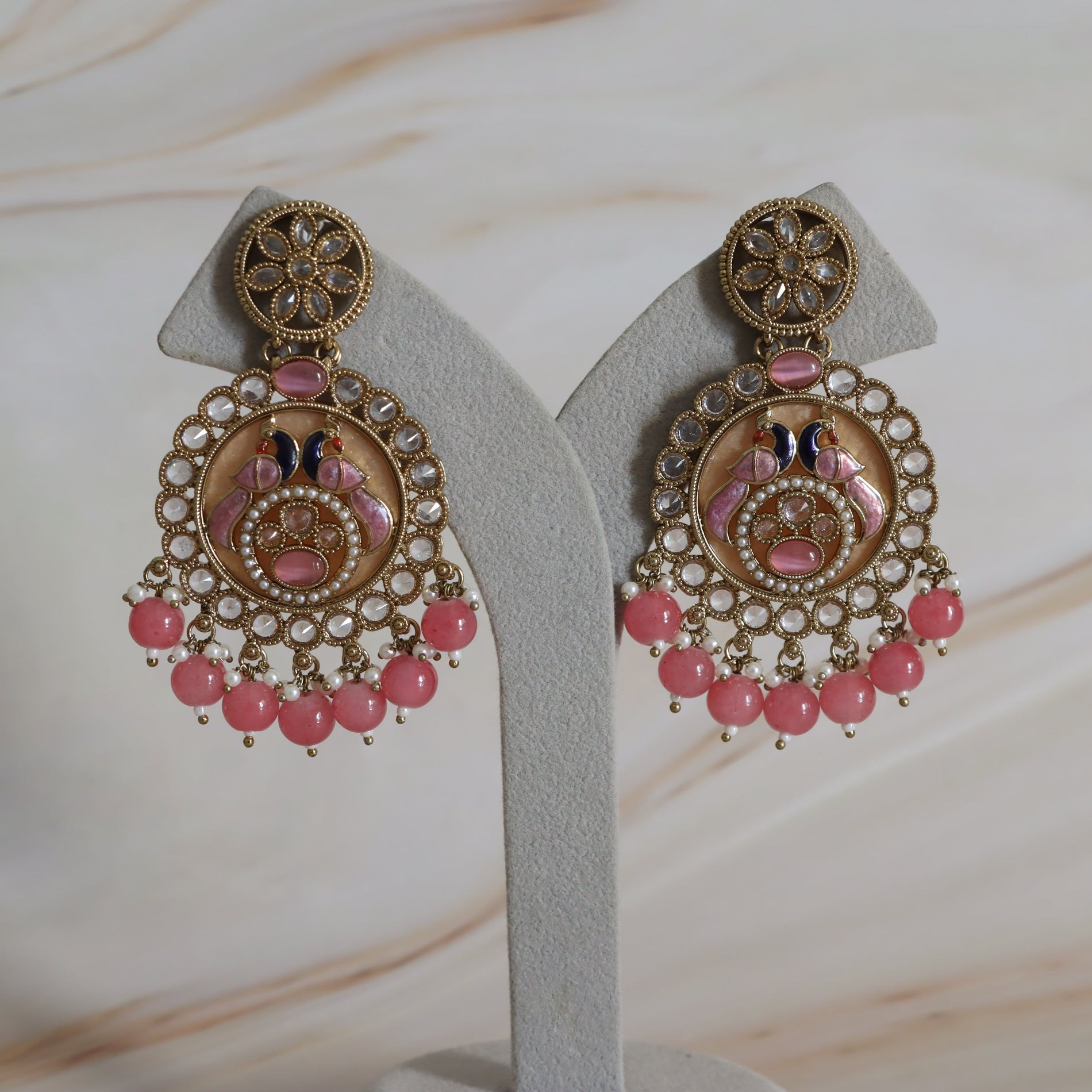 Ornate earrings with pink beads on a white stand against a marble background