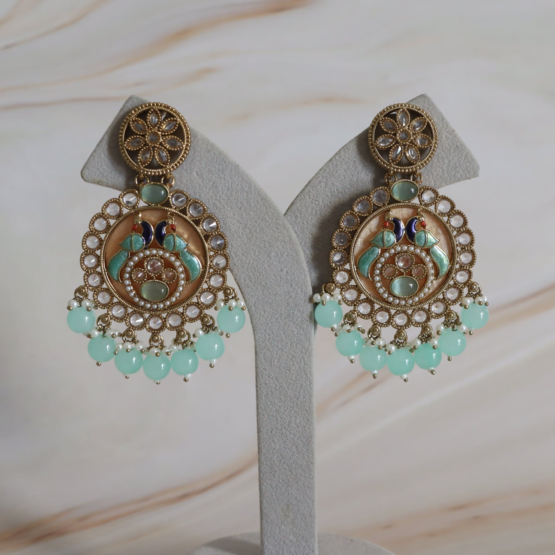 Pair of ornate earrings with gold detailing and turquoise beads on a white stand.