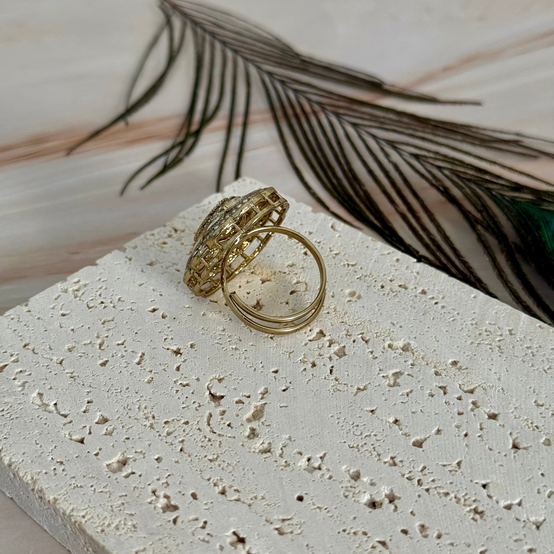 Gold ring on a textured stone surface with a feather in the background