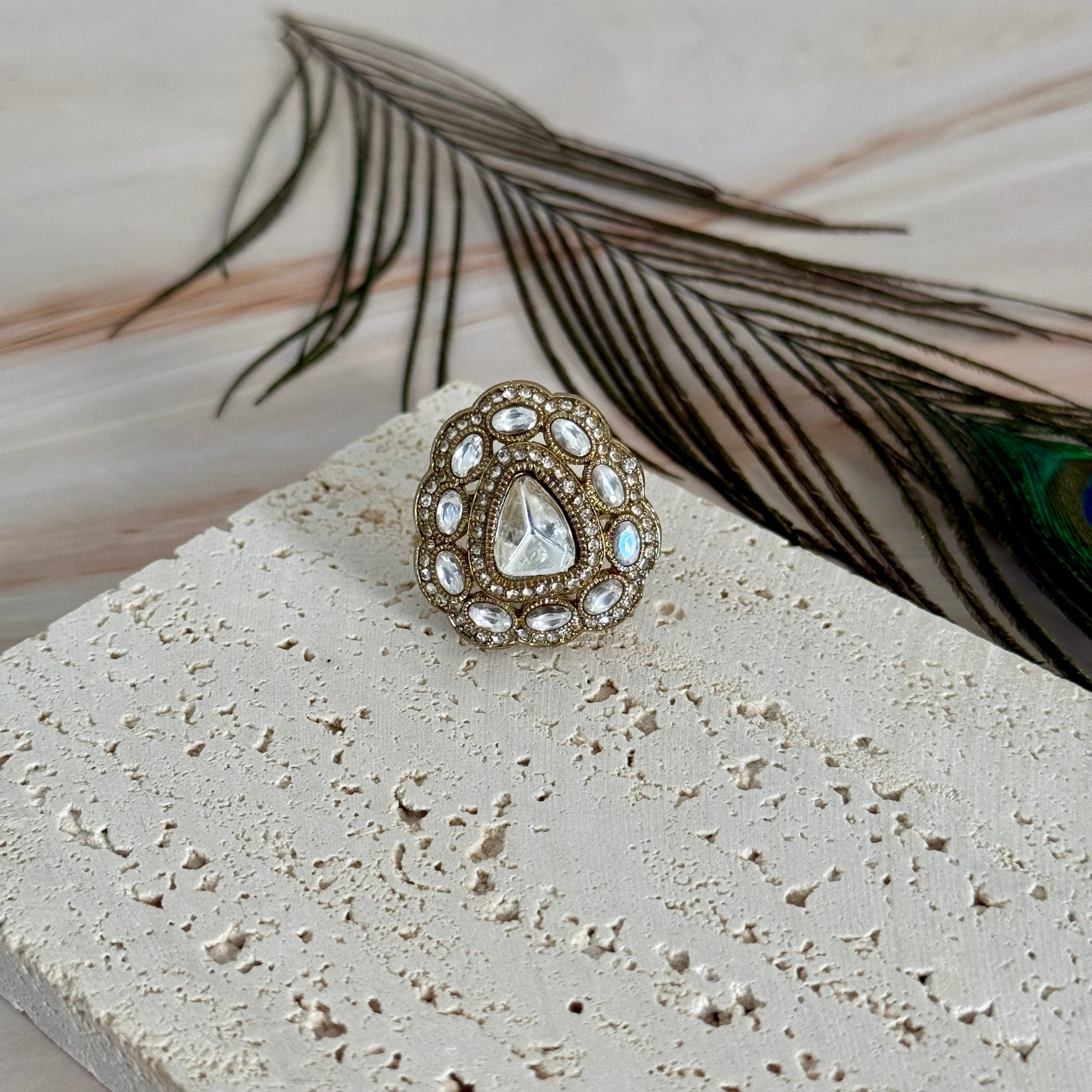 Decorative ring with gemstones on a textured surface with feathers in the background