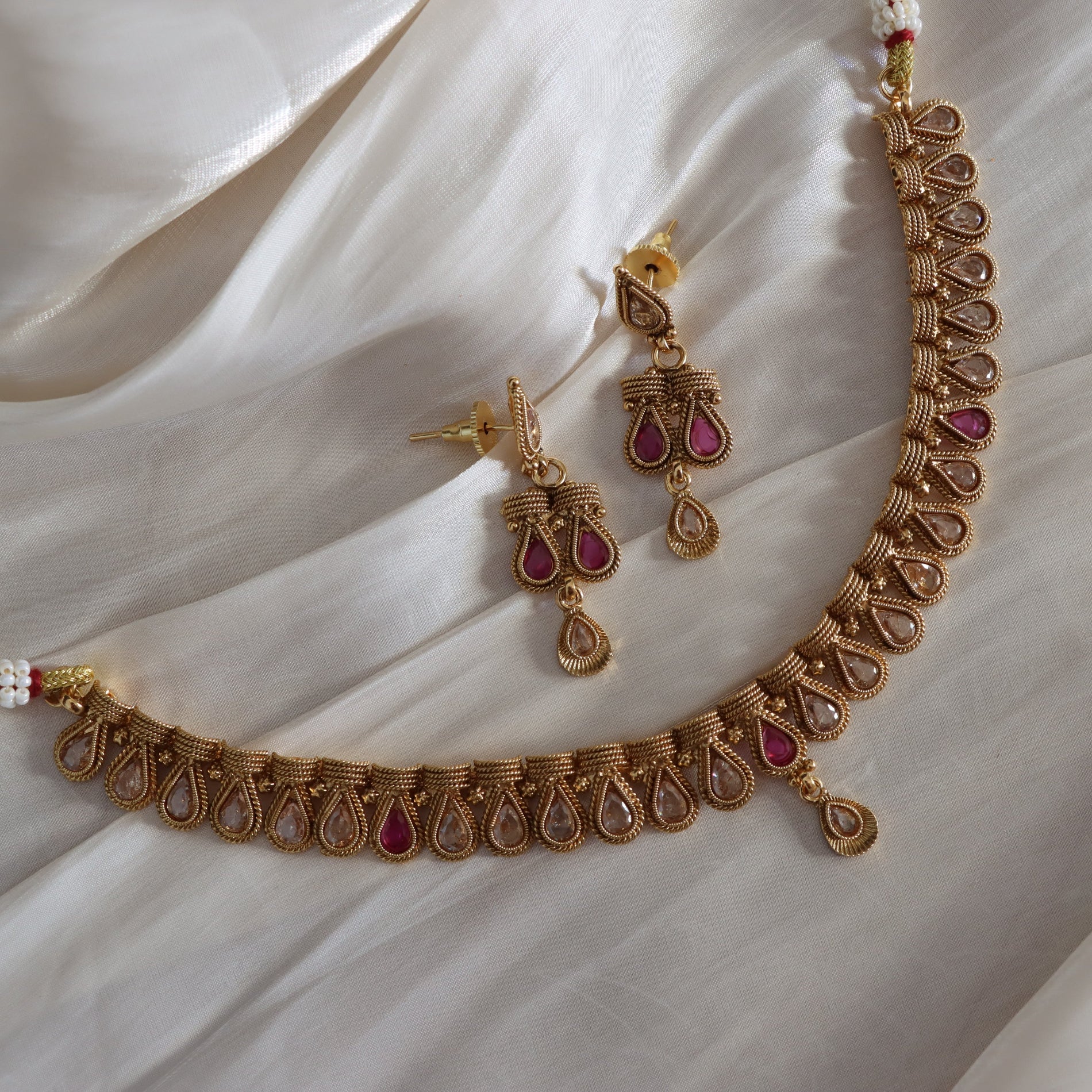 Gold necklace and earrings with pink stones on a white fabric background