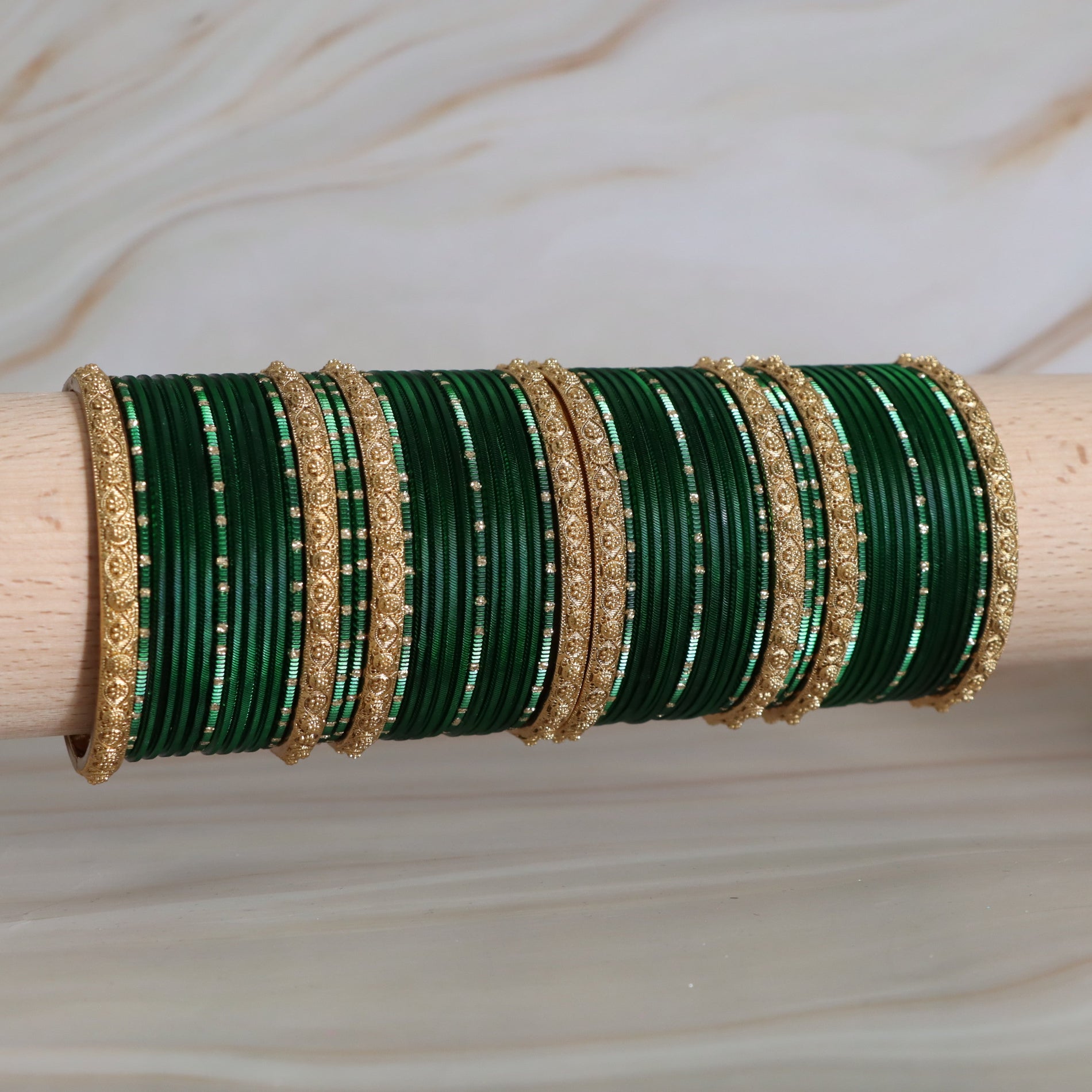 Green and gold bangles on a wooden stick against a neutral background