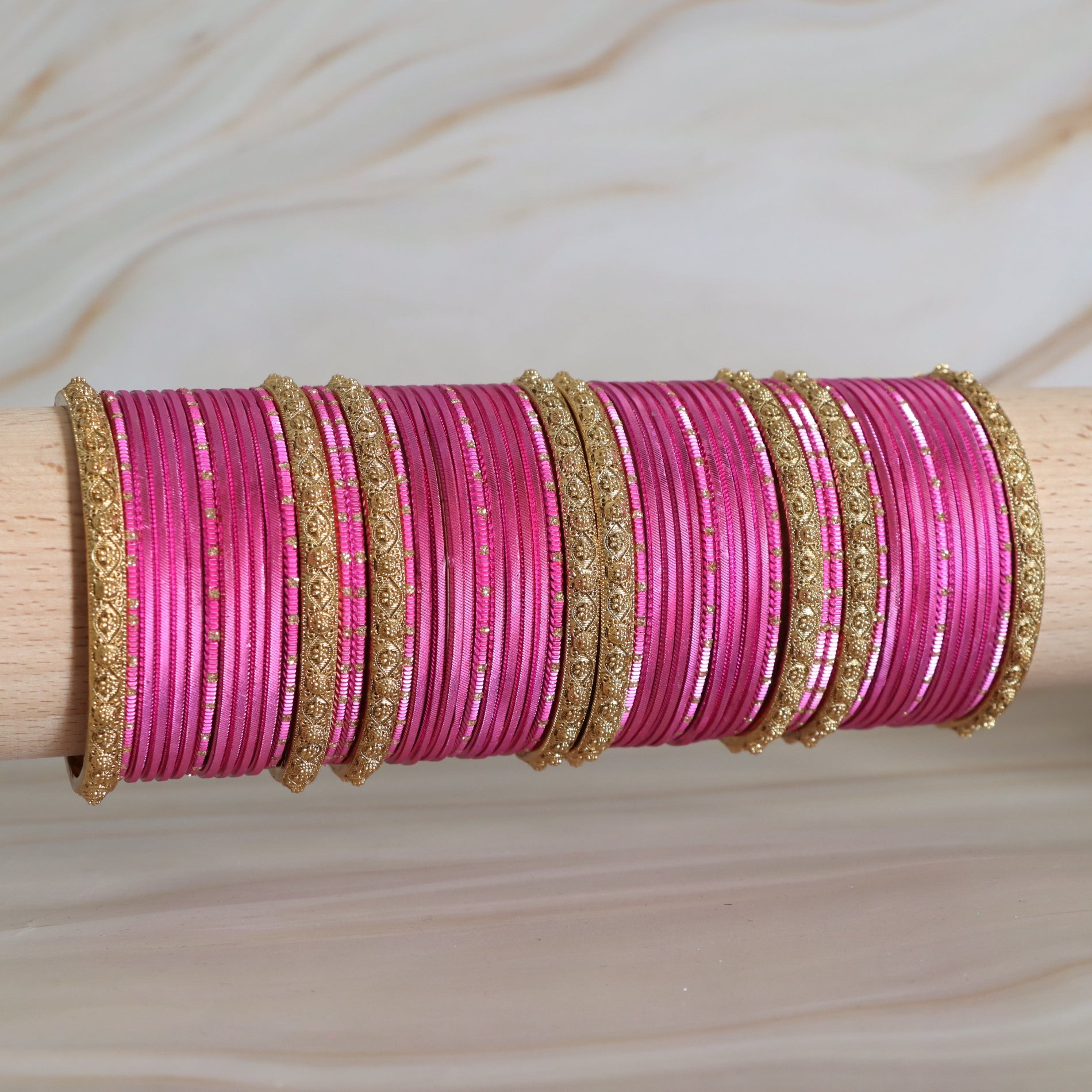 Pink bangles with gold accents on a wooden stick against a neutral background