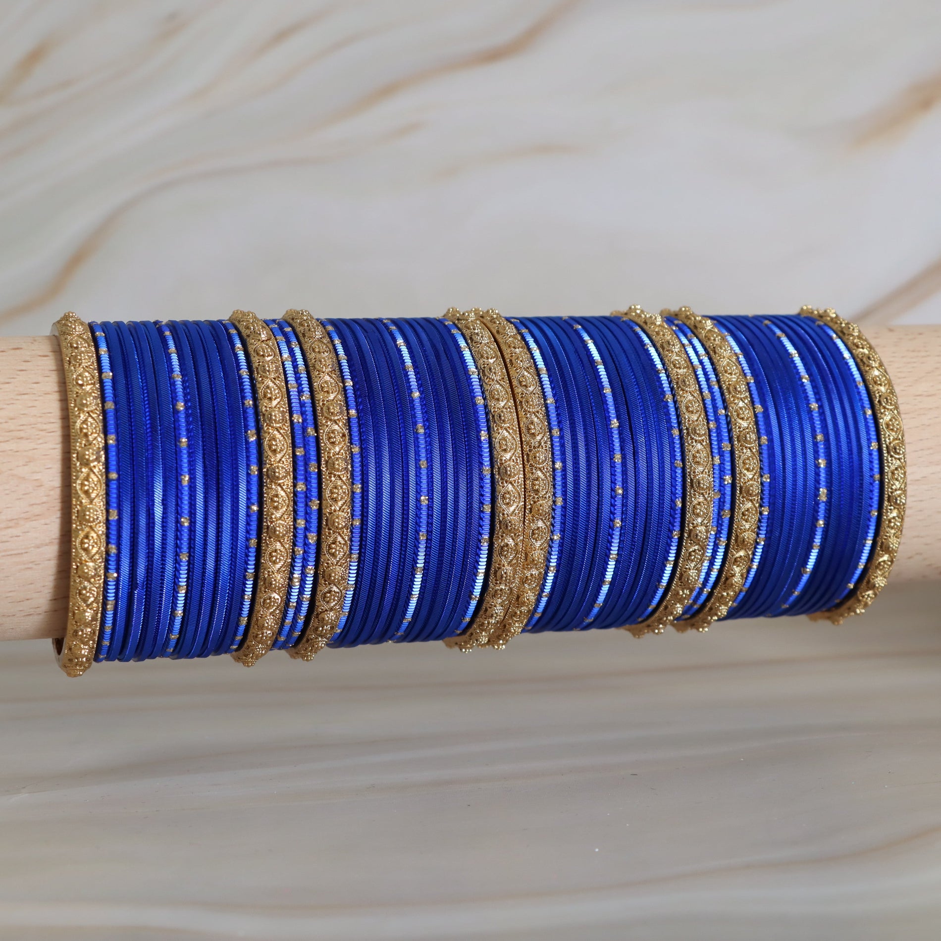 Set of blue bangles with gold accents on a wooden stick against a beige background