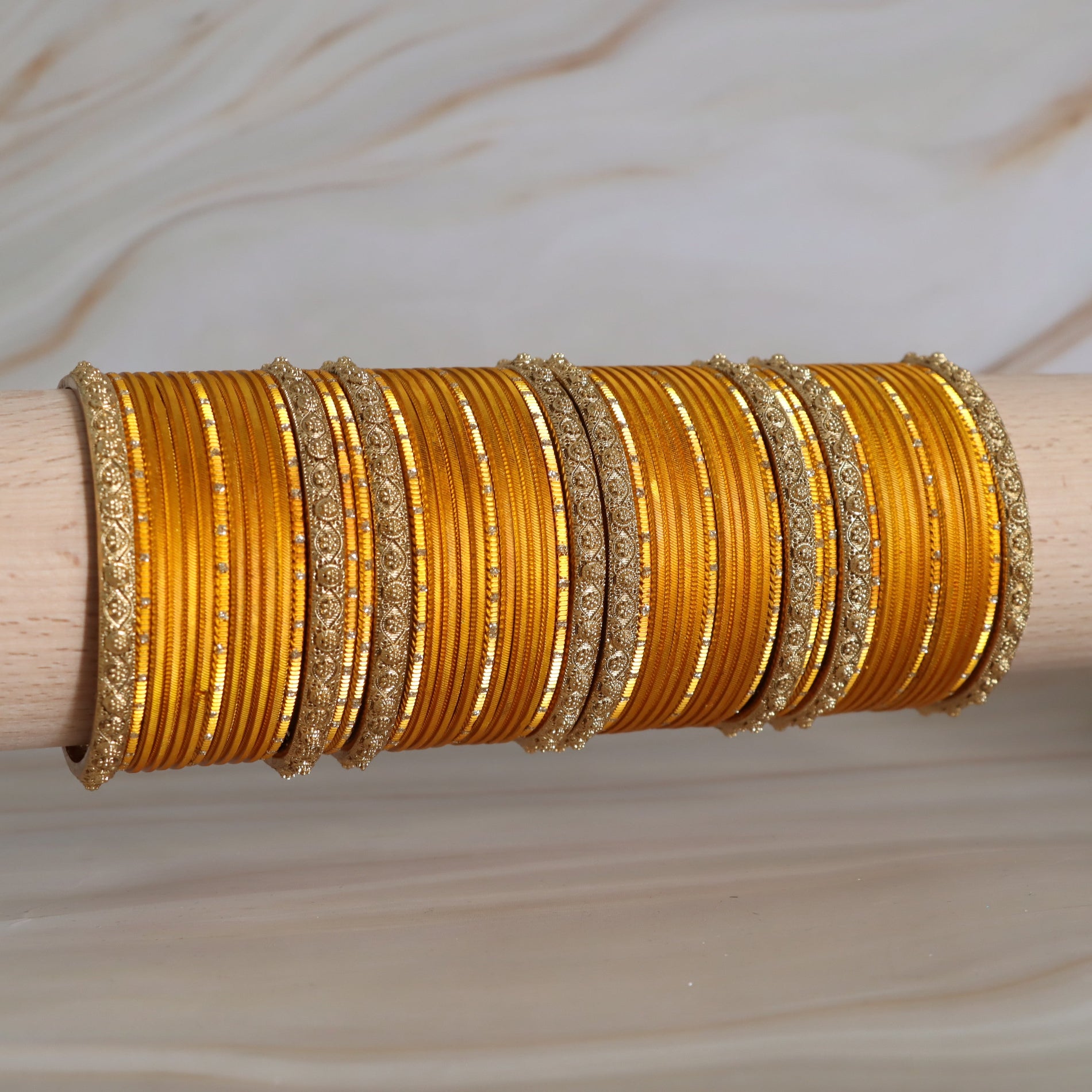 Set of gold bangles on a wooden stick against a neutral background
