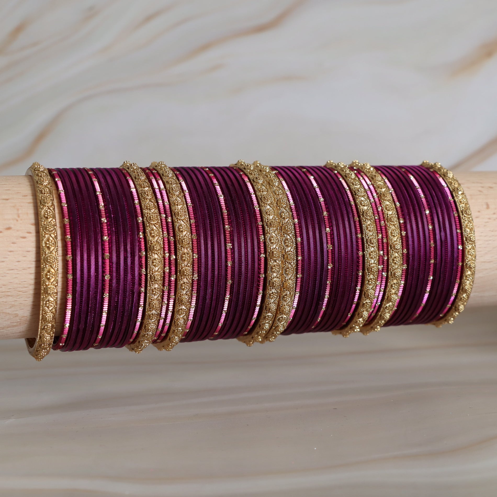 Set of purple bangles with gold accents on a wooden stick against a neutral background