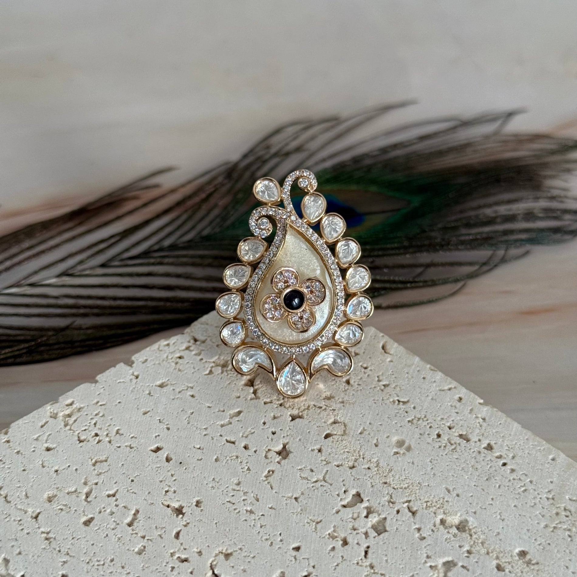 Decorative brooch with gemstones on a textured surface with peacock feathers in the background