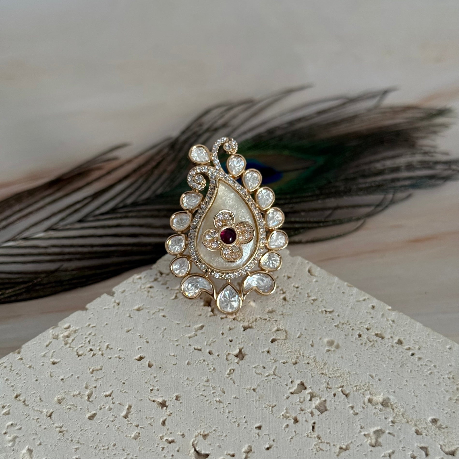 Decorative ring with gemstones on a textured surface with feathers in the background