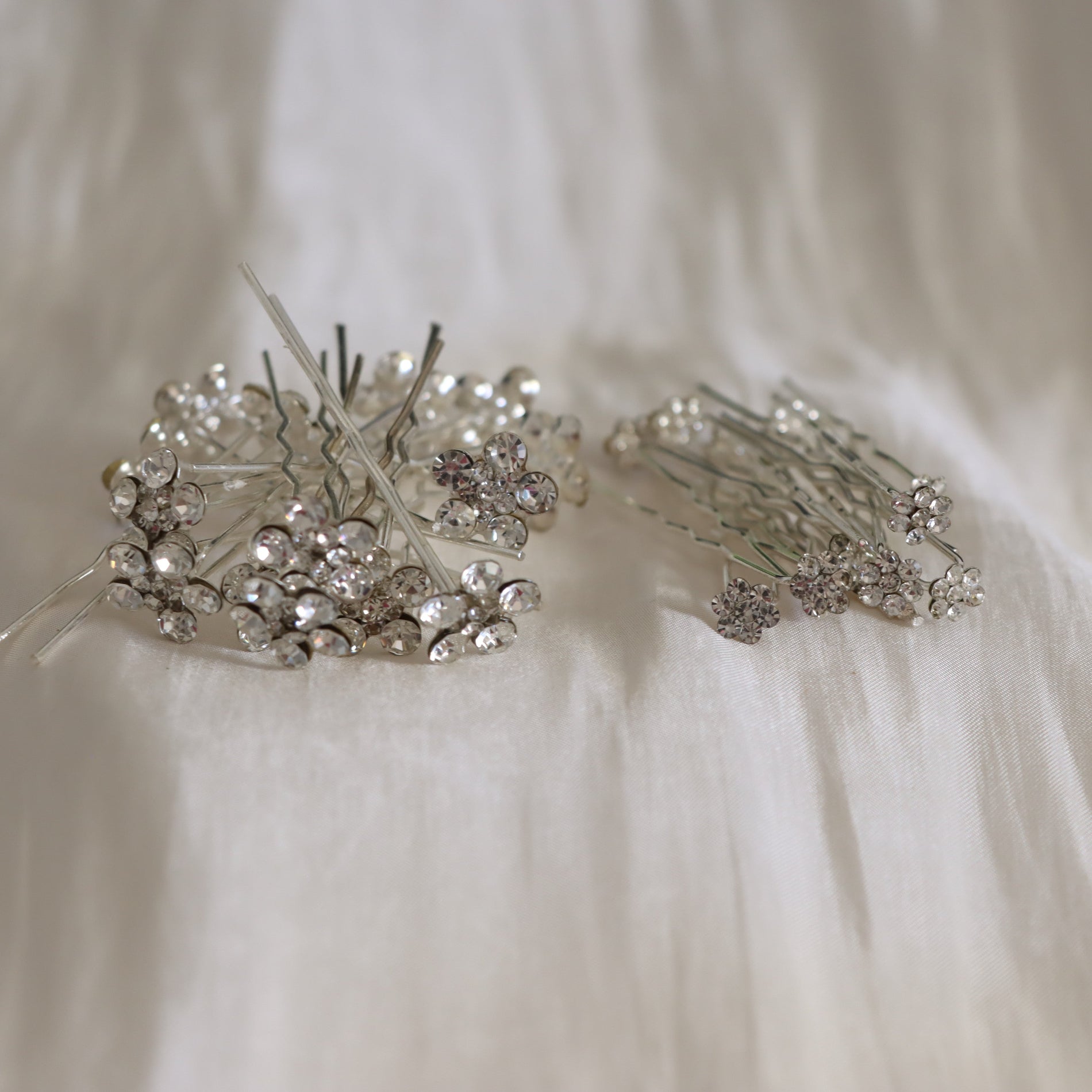 Two silver bridal hairpins decorated with clear rhinestones, displayed on a soft white fabric background.