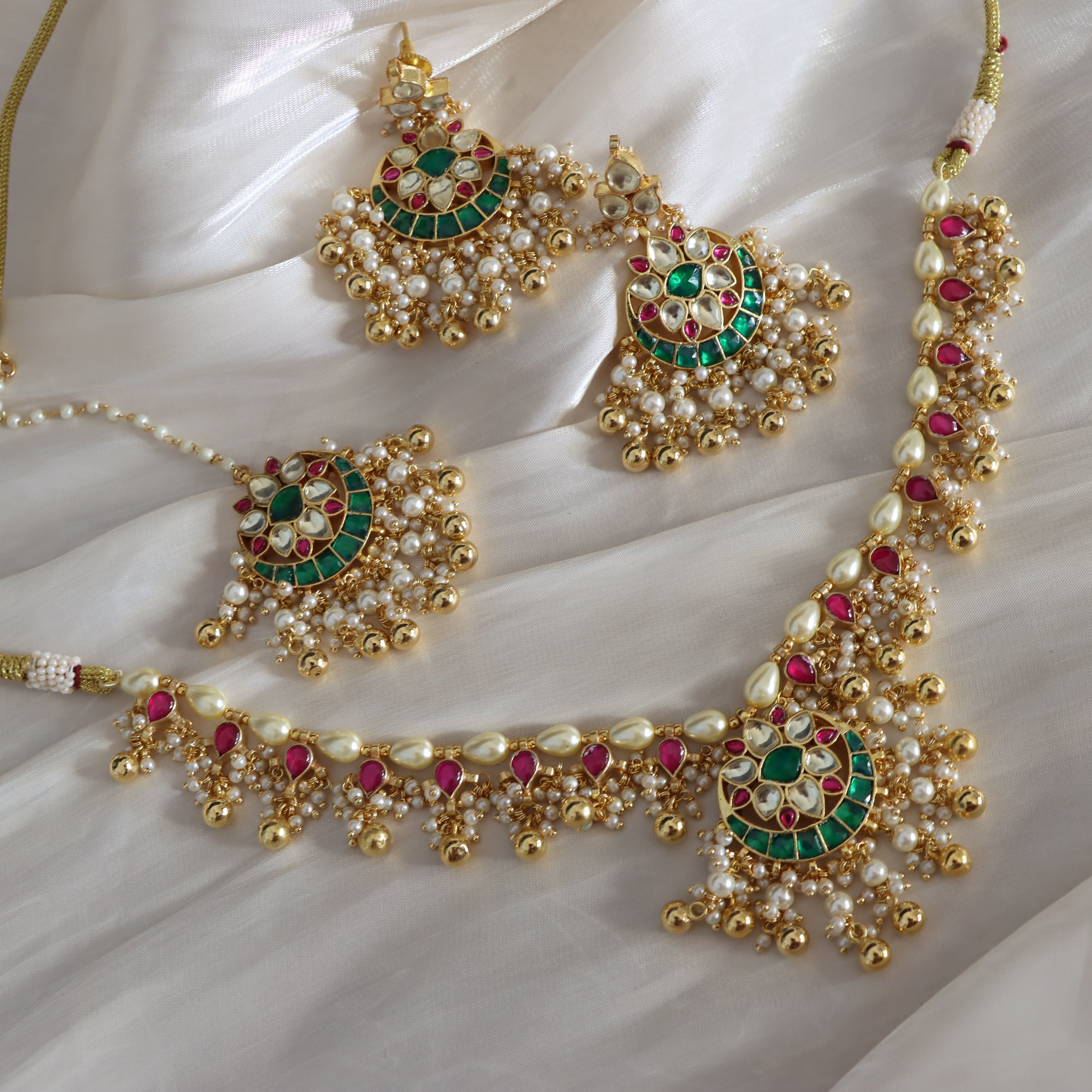 Ornate gold necklace with pearls and gemstones on a white fabric background