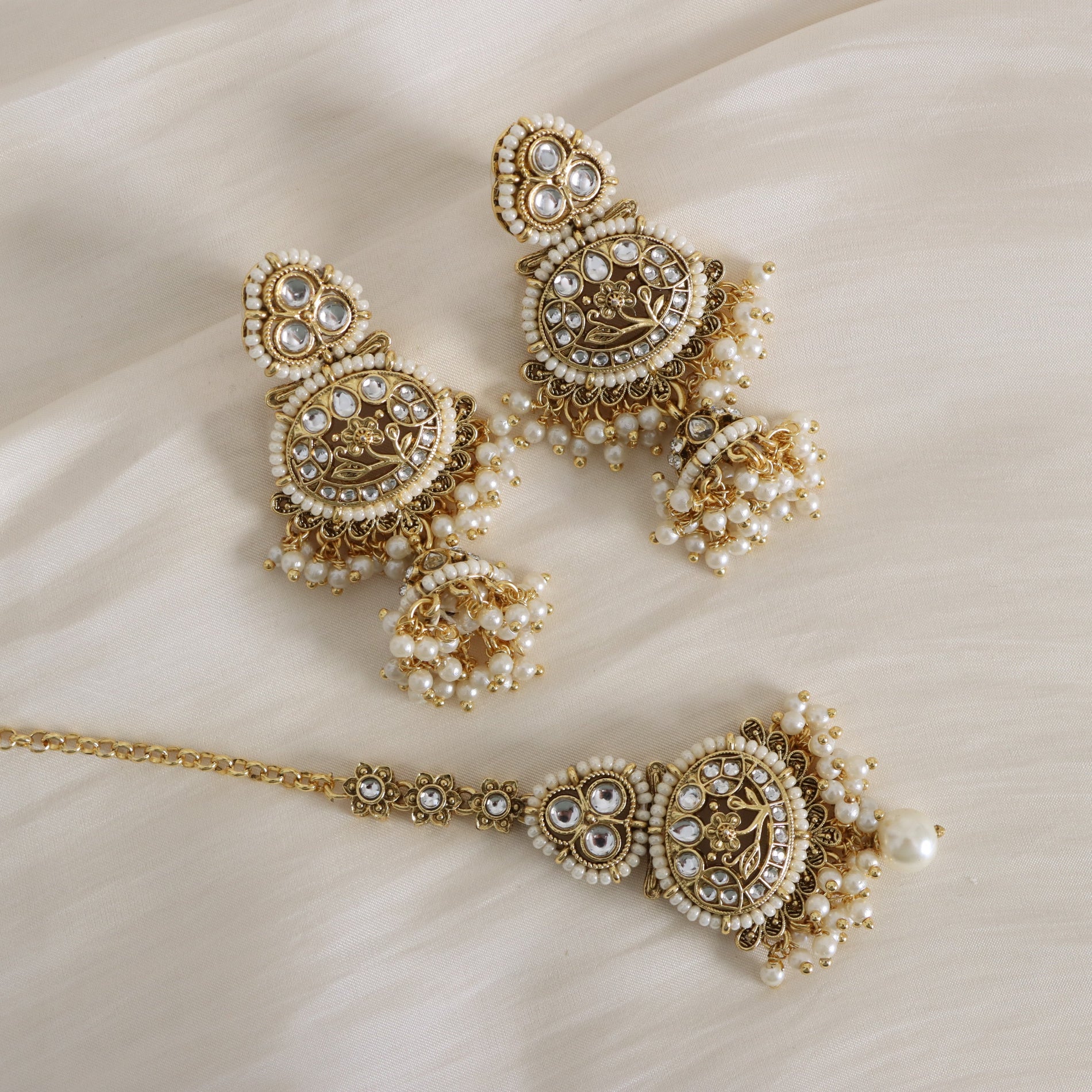 Ornate gold and pearl jewelry set on a beige fabric background