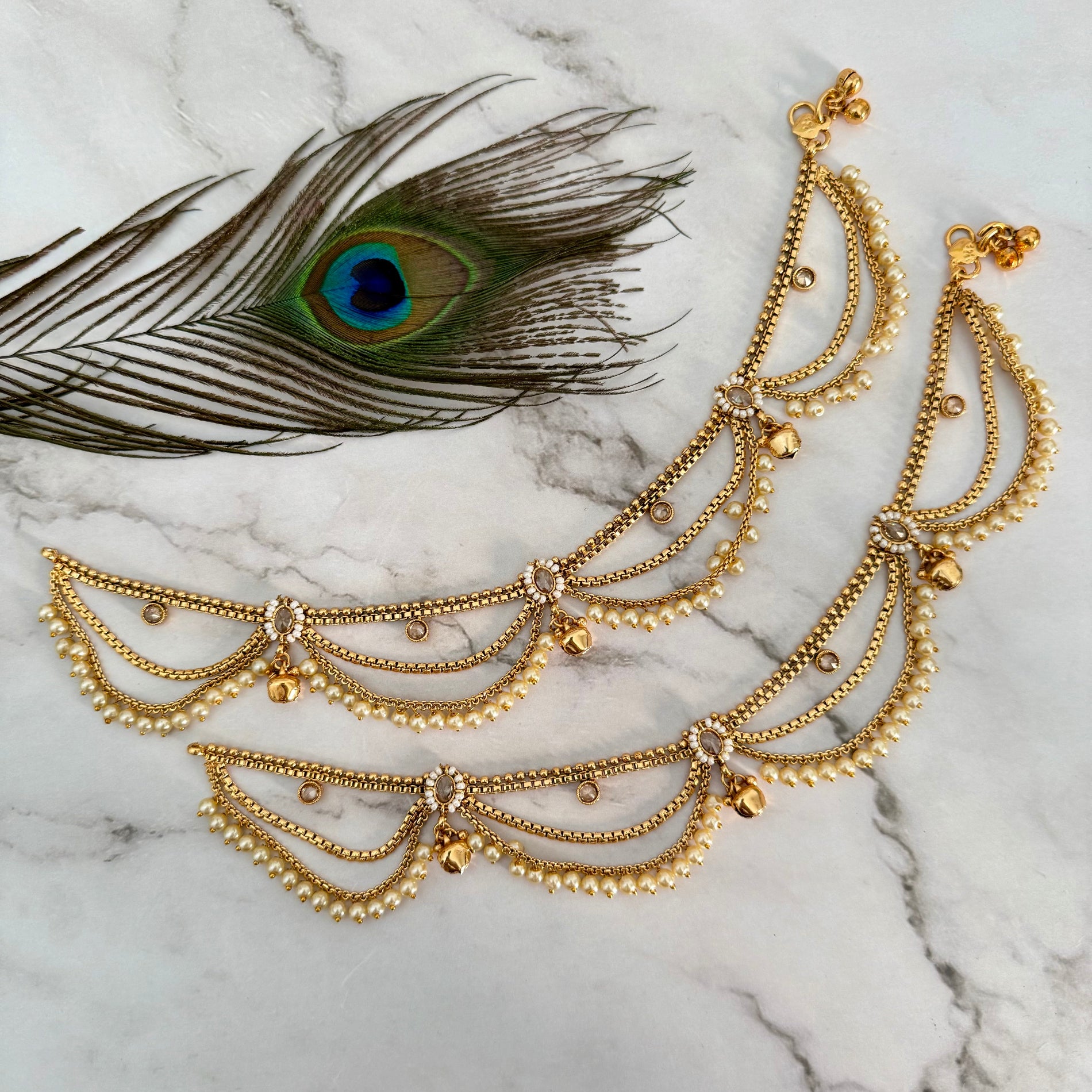Gold anklet with peacock feather on marble background
