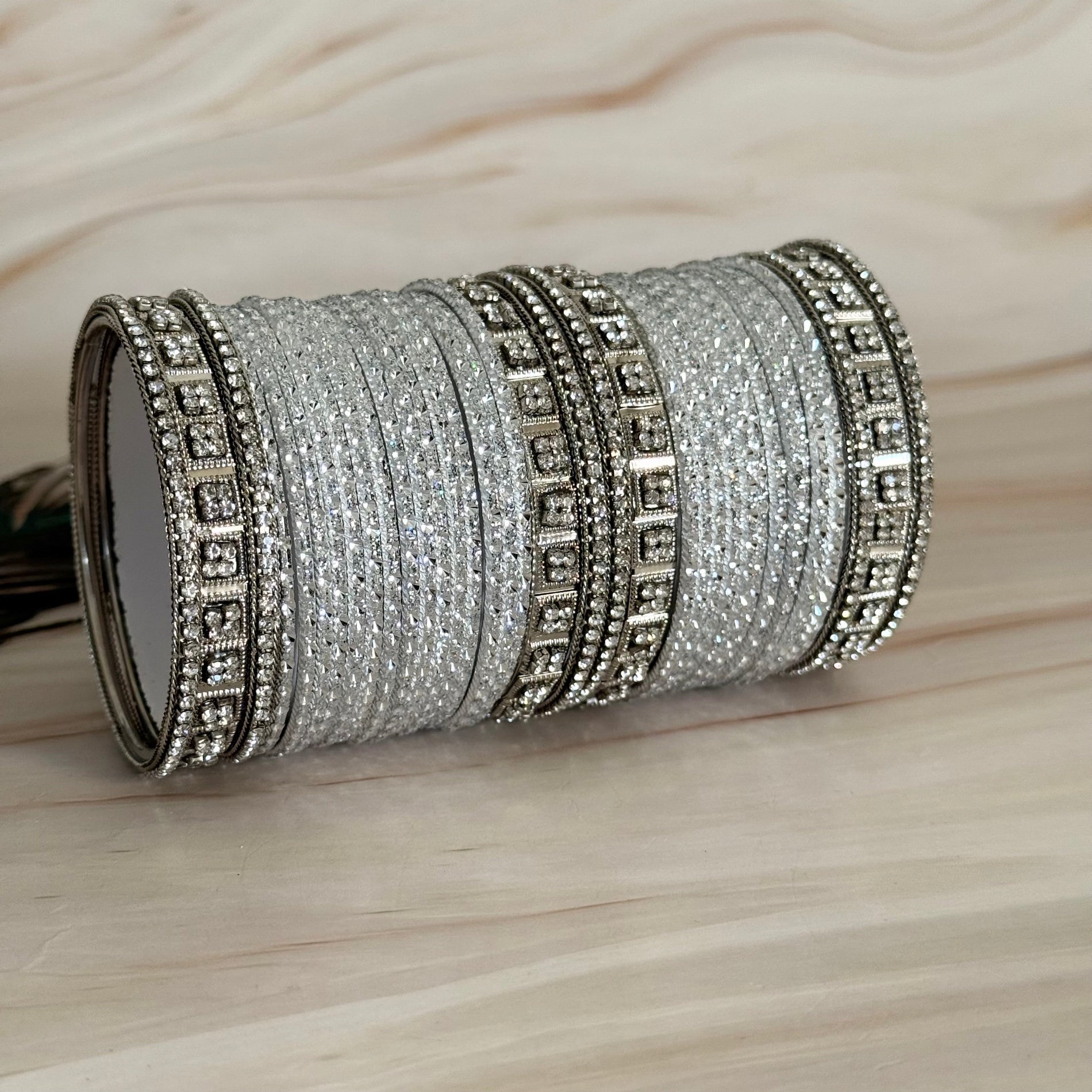 Set of silver bangles with intricate designs on a wooden surface