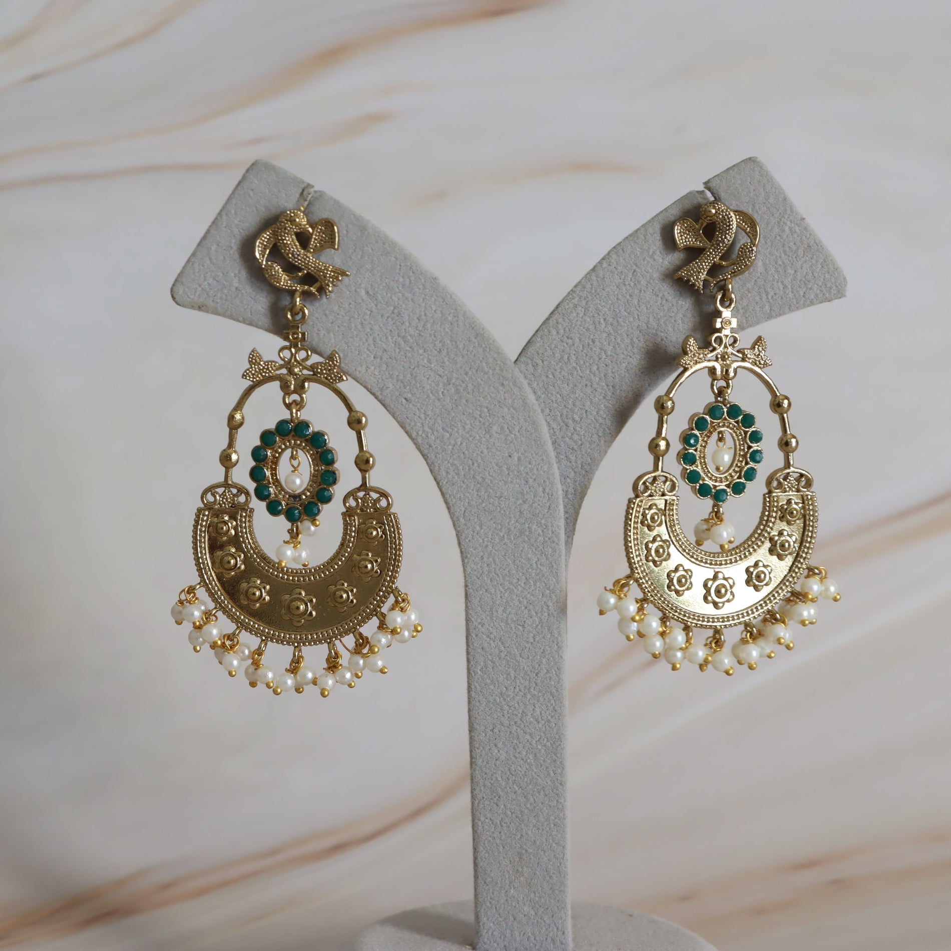 Pair of gold and green earrings on a gray stand with a neutral background