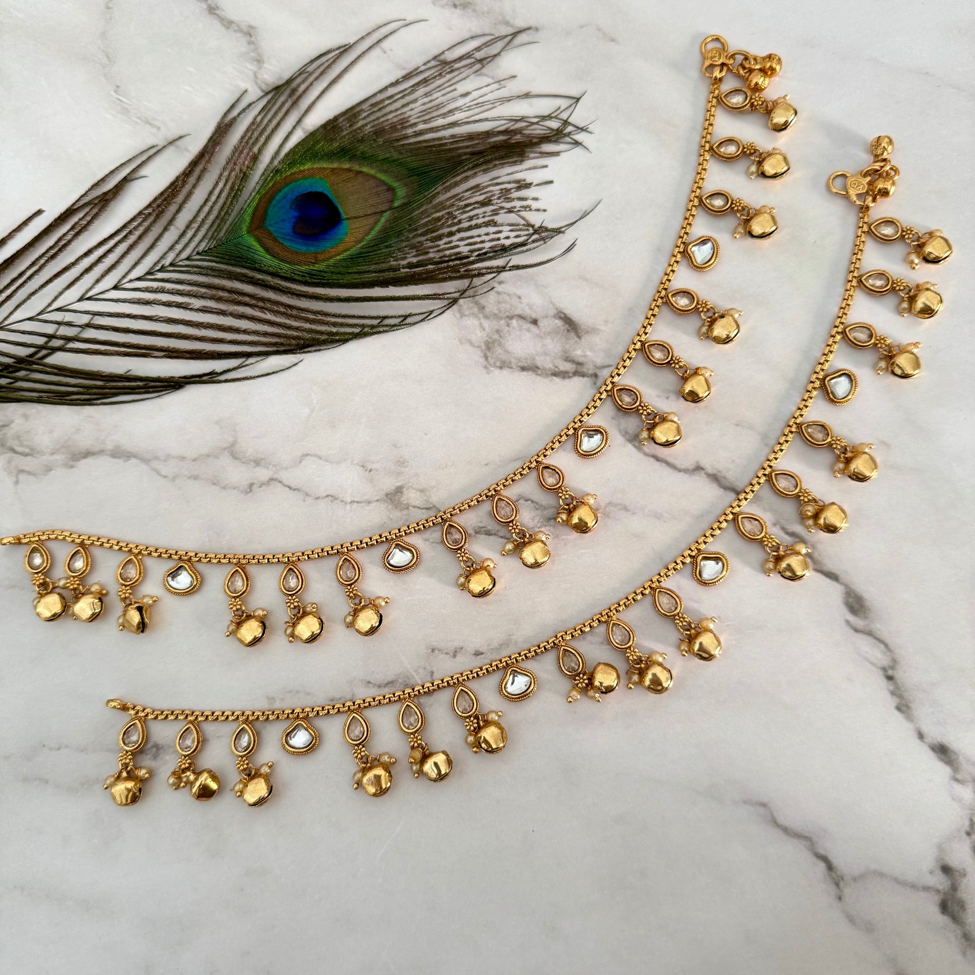 Gold anklet with peacock feather on marble background