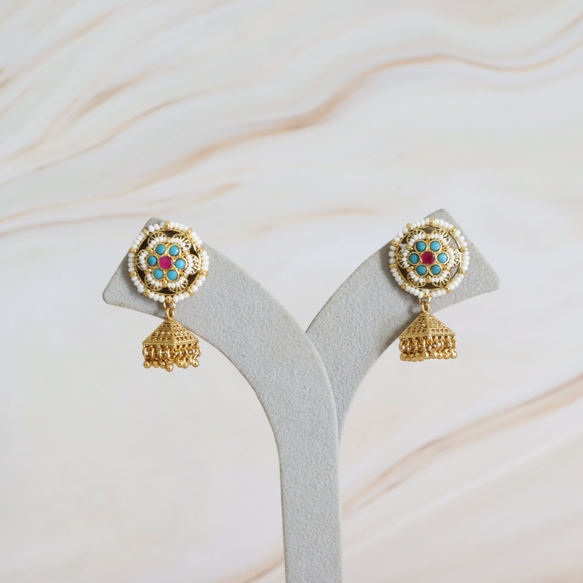 Gold earrings with colorful gemstones on a gray stand against a marble background