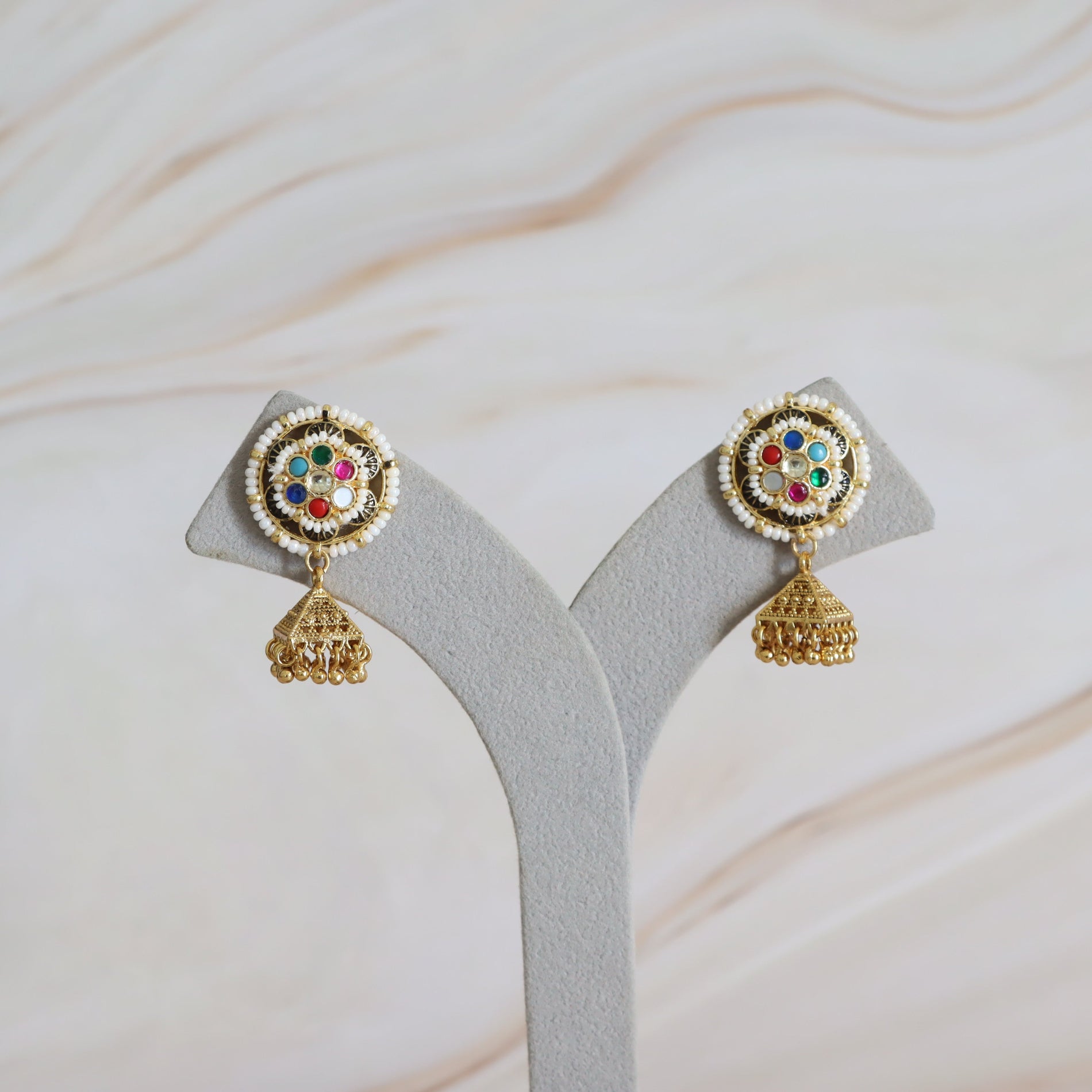Pair of gold earrings with colorful gemstones on a gray stand against a marble background