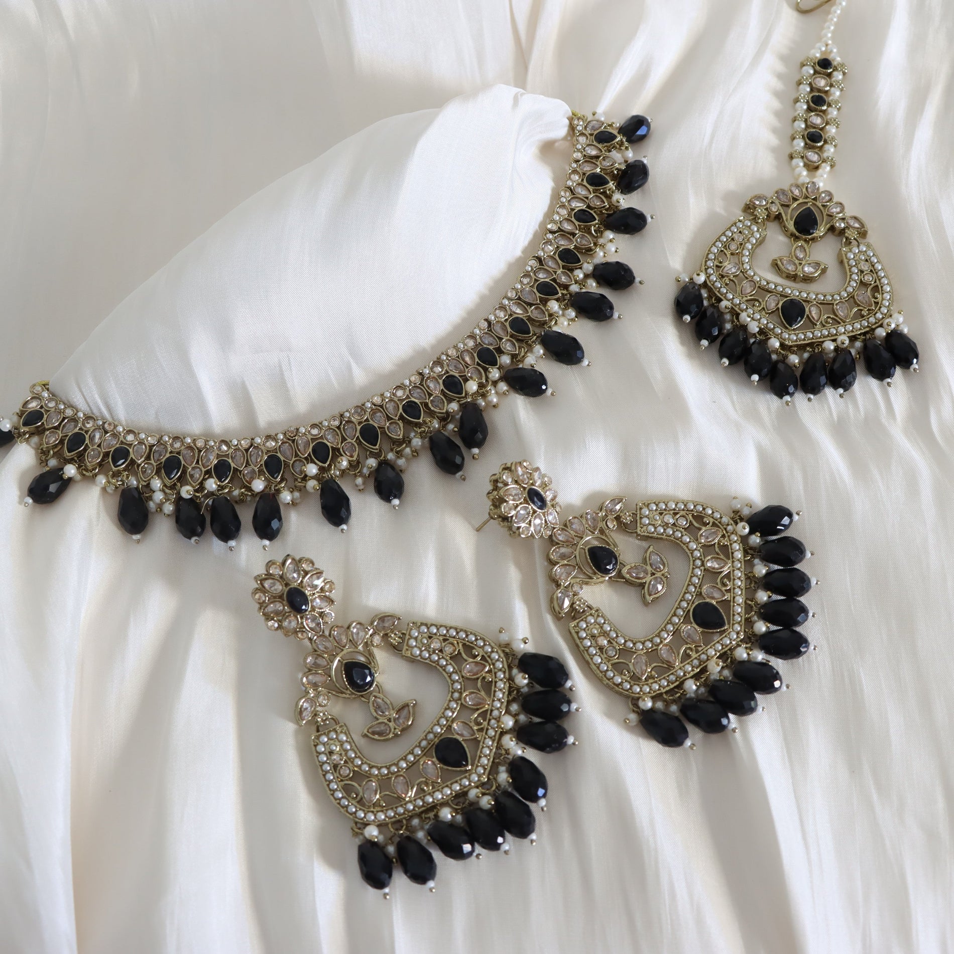 Ornate necklace and earrings with black stones on a white fabric background