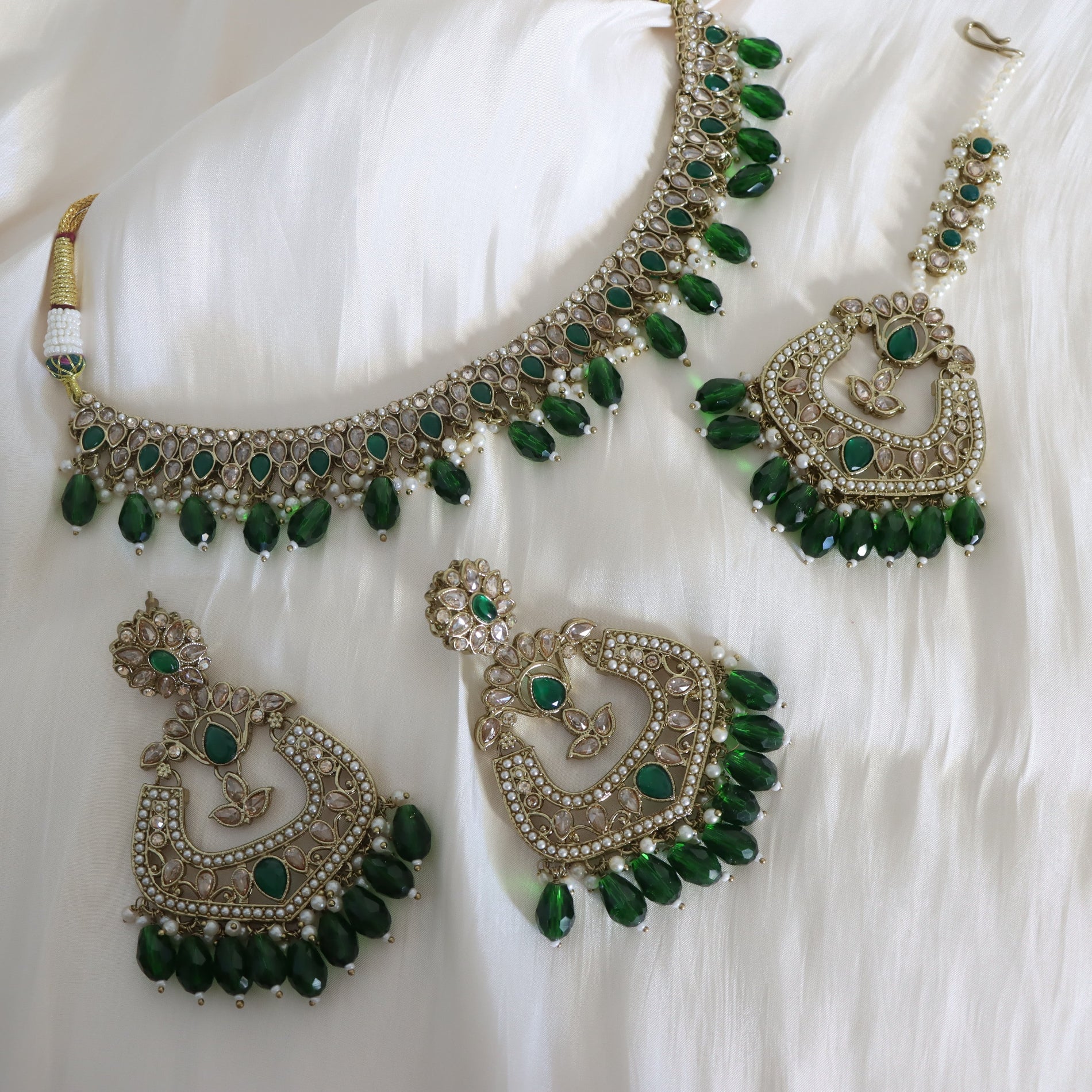 Ornate necklace and earrings with green gemstones on a white fabric background