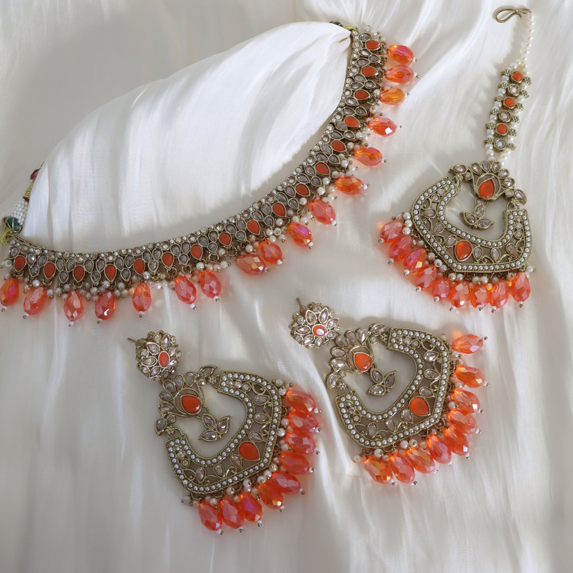 Ornate jewelry set with orange beads on a white fabric background