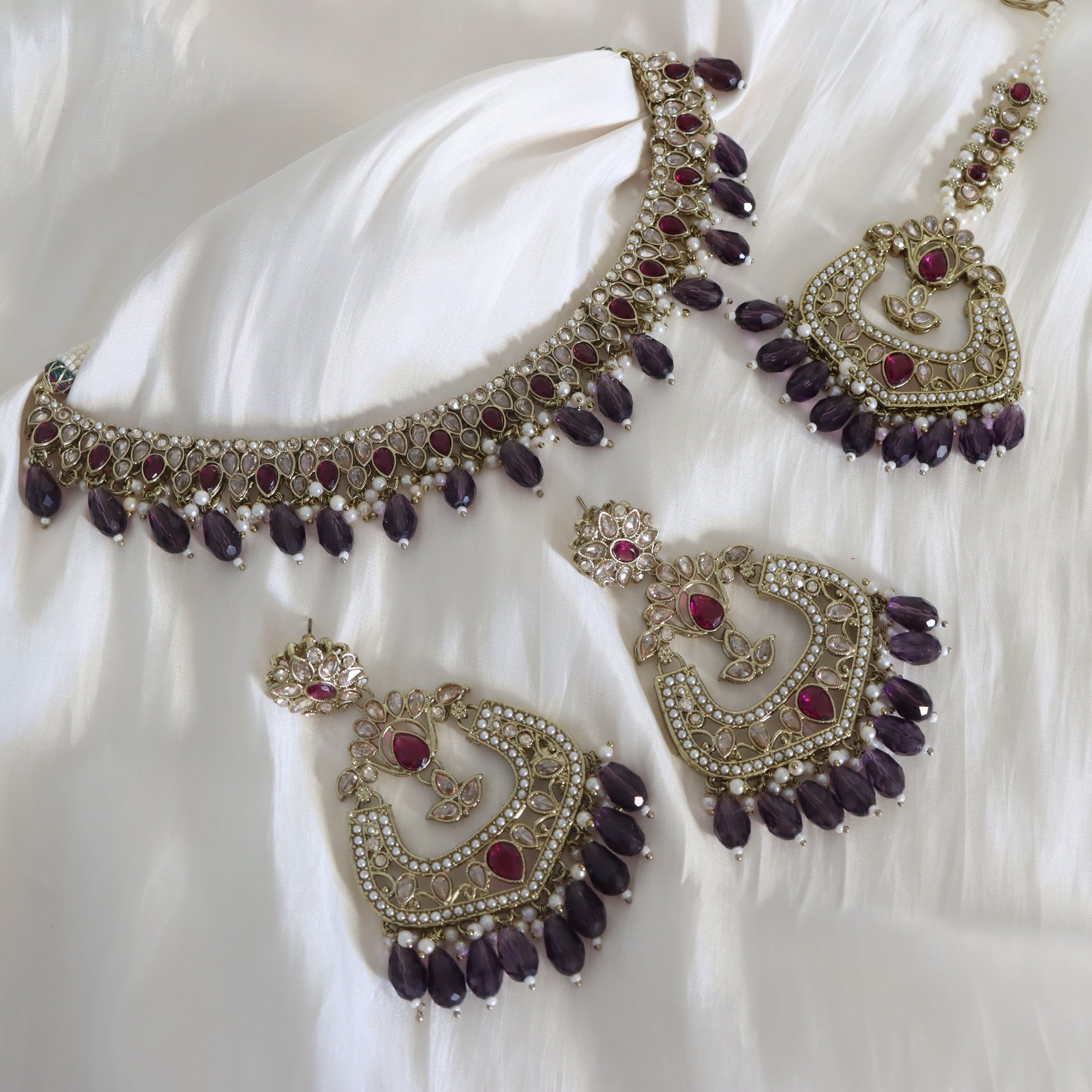 Ornate jewelry set with purple stones on a white fabric background