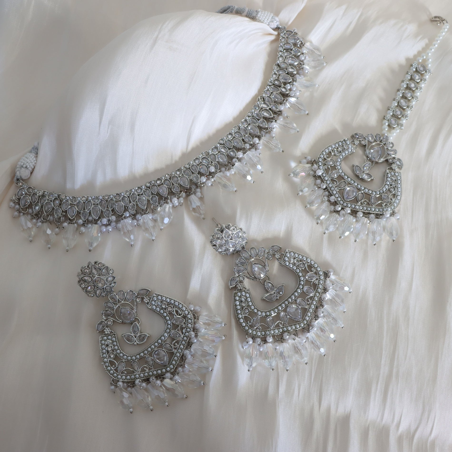 Silver jewelry set with necklace and earrings on a white fabric background