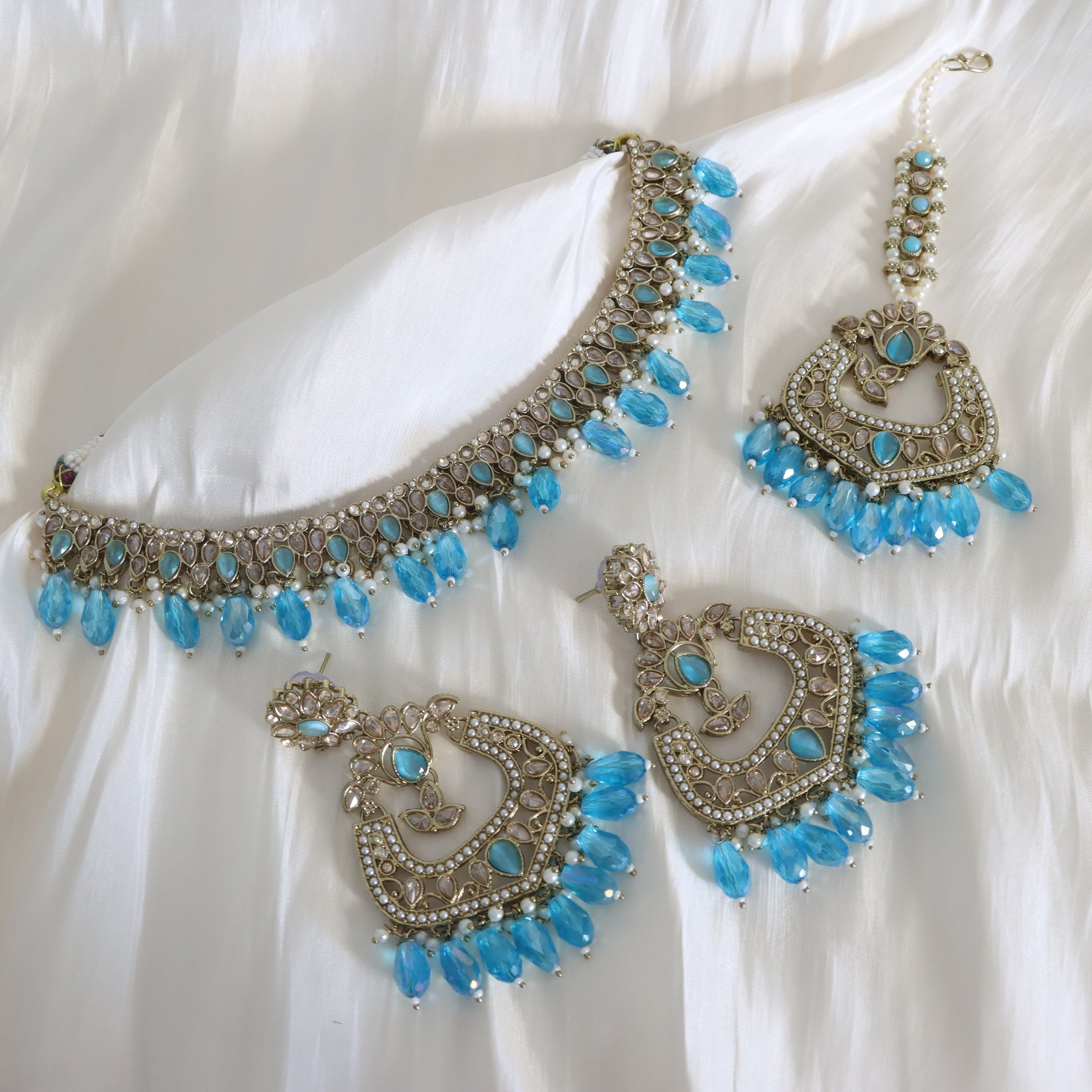 Jewelry set with necklace and earrings featuring blue stones on a white fabric background